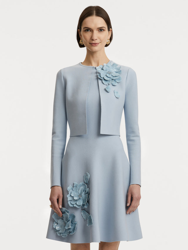 Front view of model wearing a cropped overlayer in light blue with sequin peony appliqués at the neckline. 