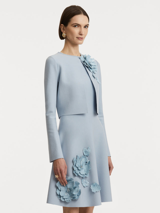 Side view of model wearing a cropped overlayer in light blue with sequin peony appliqués at the neckline. 