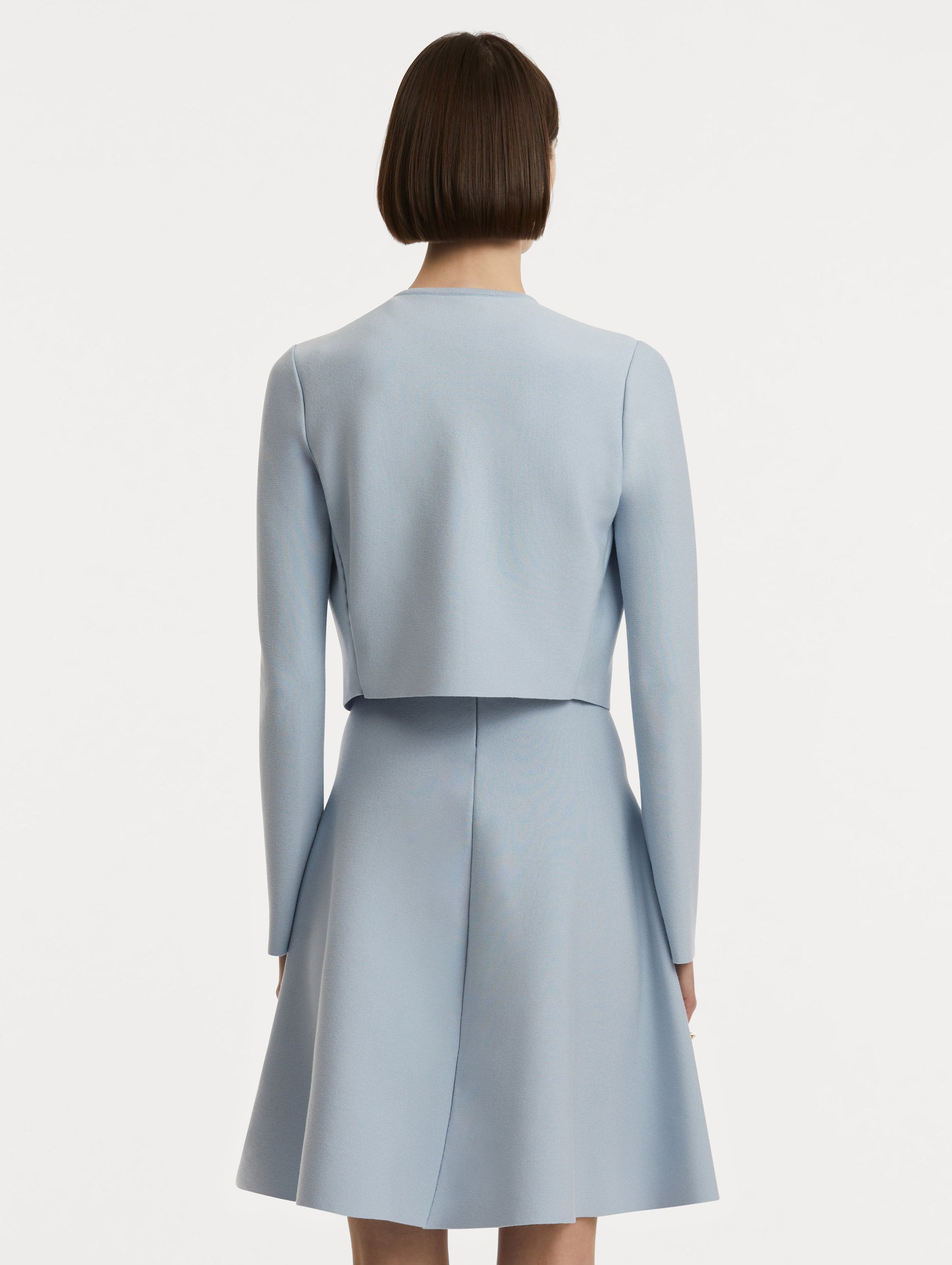 Back view of model wearing a cropped overlayer in light blue.