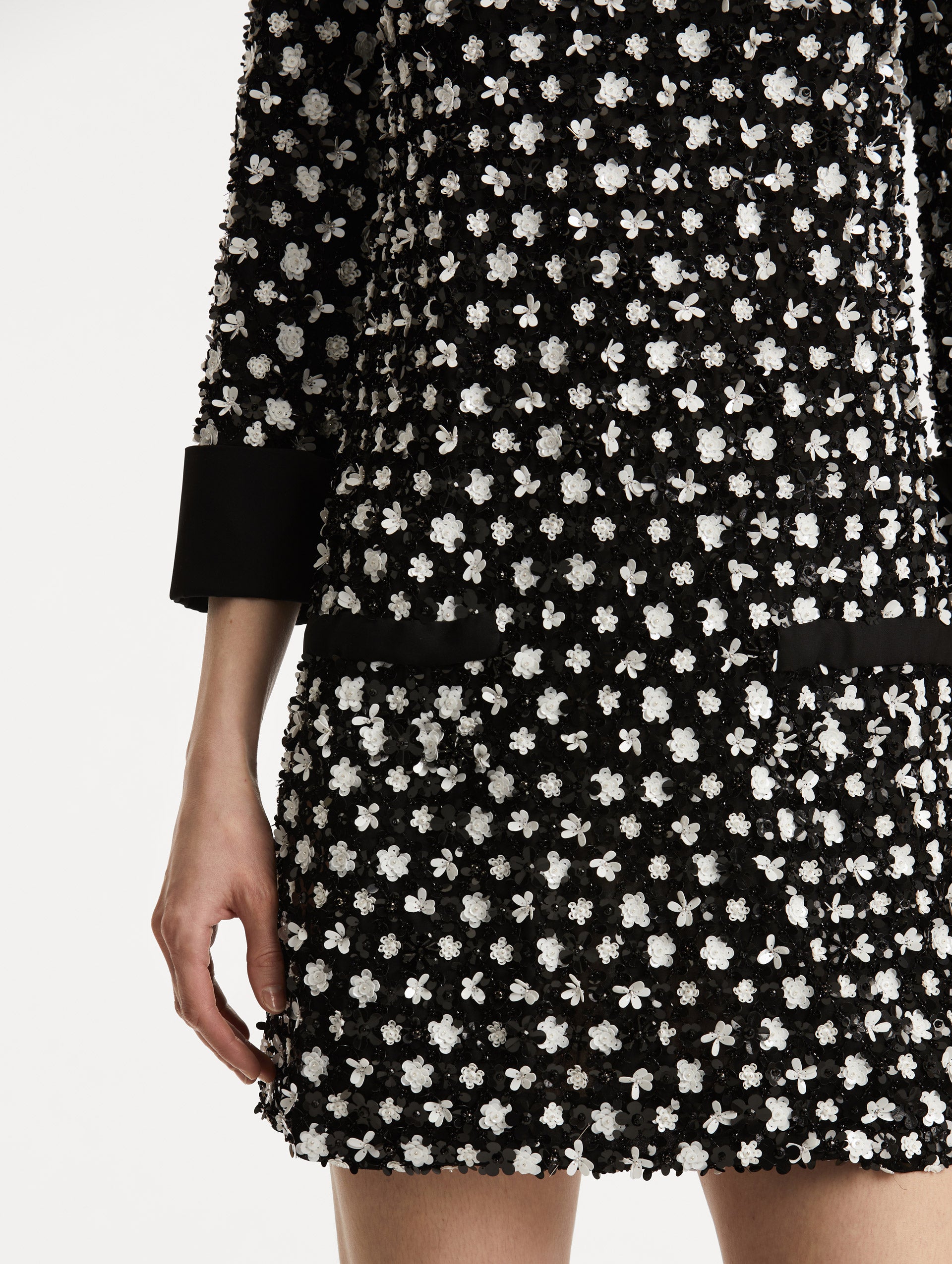 Zoomed in image of black cuffs and black non functional buttons with black and ivory floral sequin embroidery. 