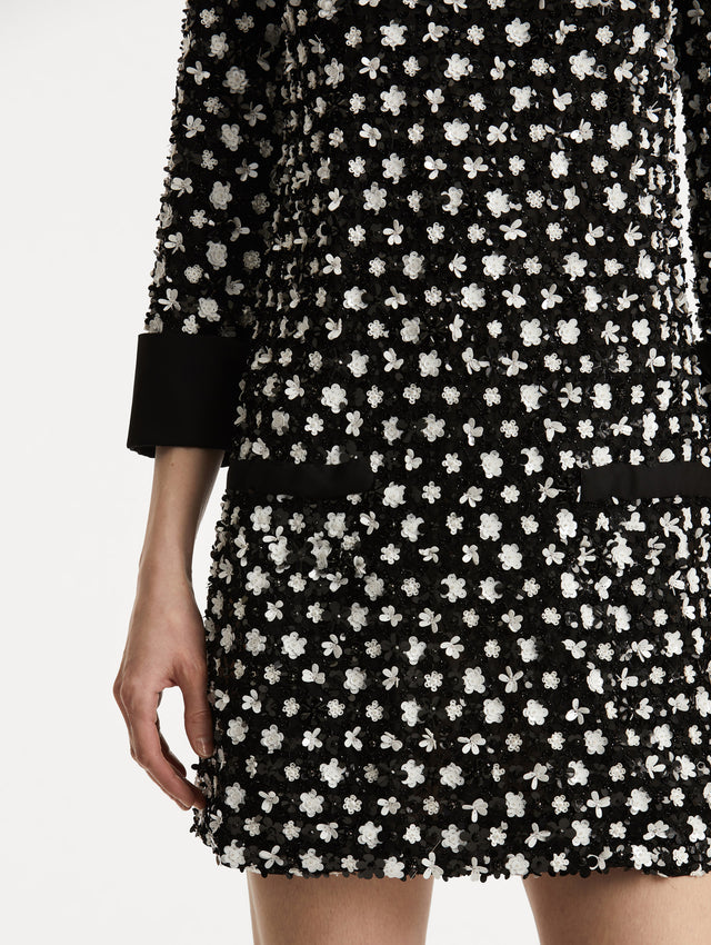 Zoomed in image of black cuffs and black non functional buttons with black and ivory floral sequin embroidery. 