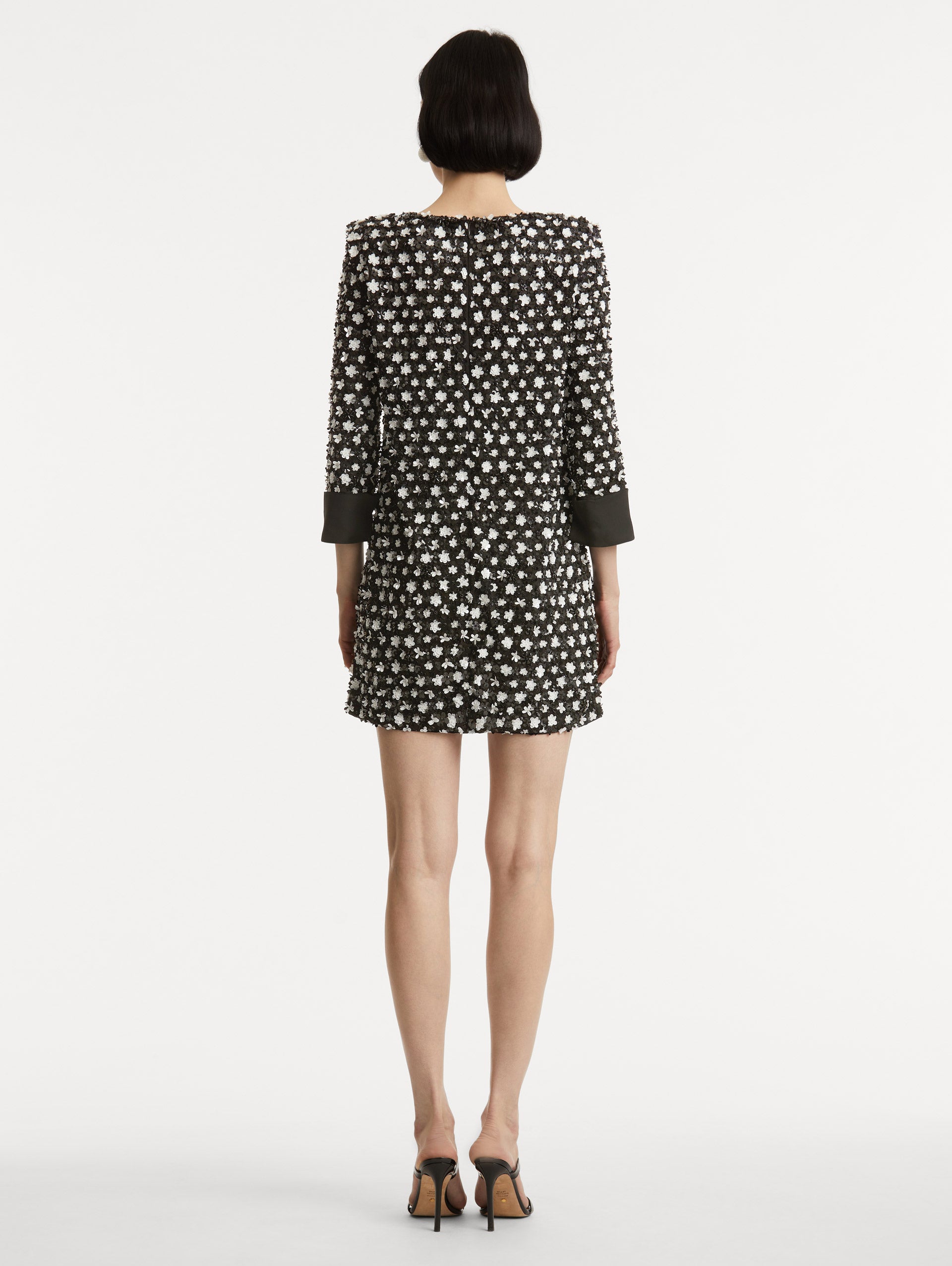 Full body back view of model wearing dress with black and ivory floral sequin embroidery across the dress with three-quarter length sleeves with black cuffs.  