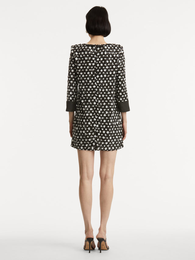Full body back view of model wearing dress with black and ivory floral sequin embroidery across the dress with three-quarter length sleeves with black cuffs.  