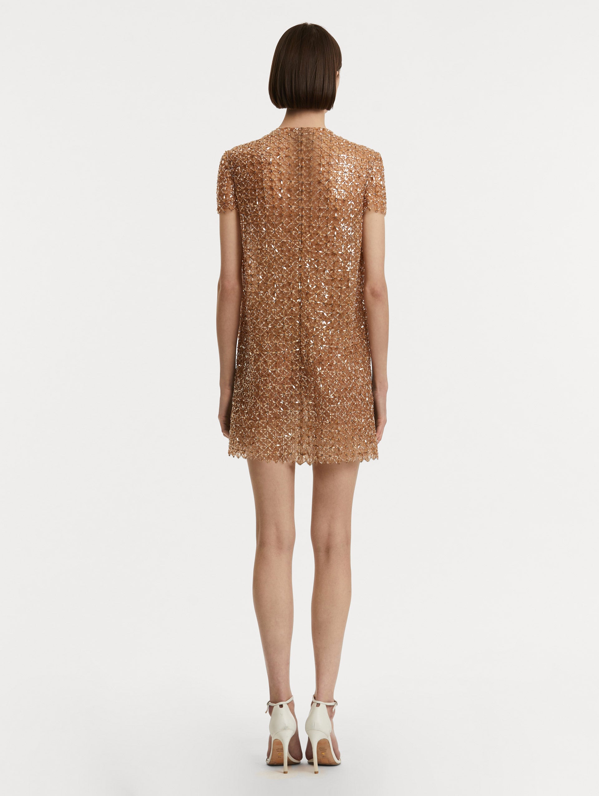 Full body back view of model wearing short sleeve dress with amber glass blooms in a grid pattern. 