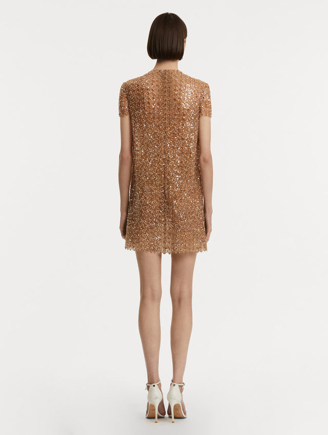 Full body back view of model wearing short sleeve dress with amber glass blooms in a grid pattern. 