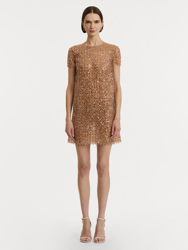 Full body front view of model wearing short sleeve dress with amber glass blooms in a grid pattern. 