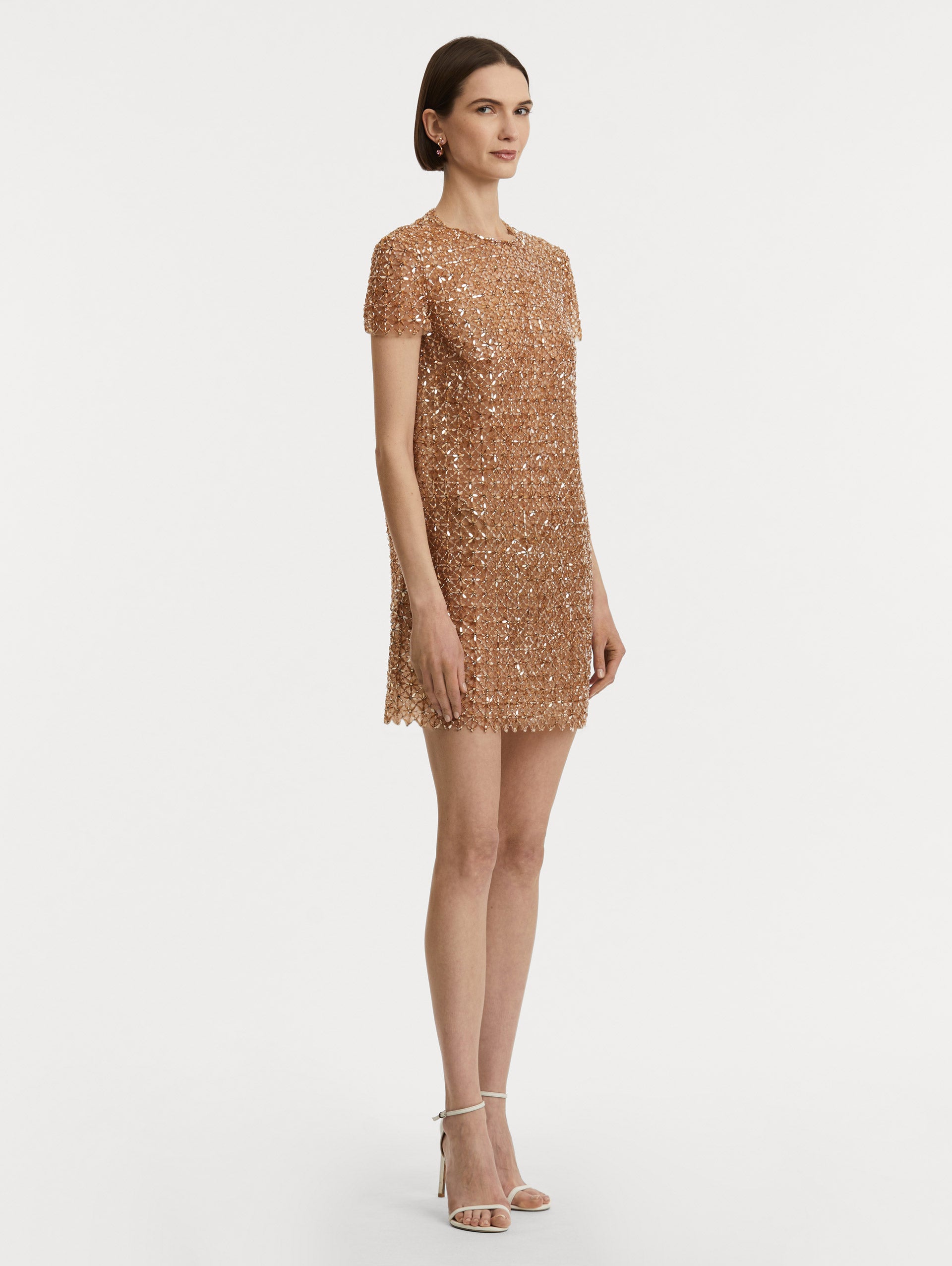 Full body side view of model wearing short sleeve dress with amber glass blooms in a grid pattern. 