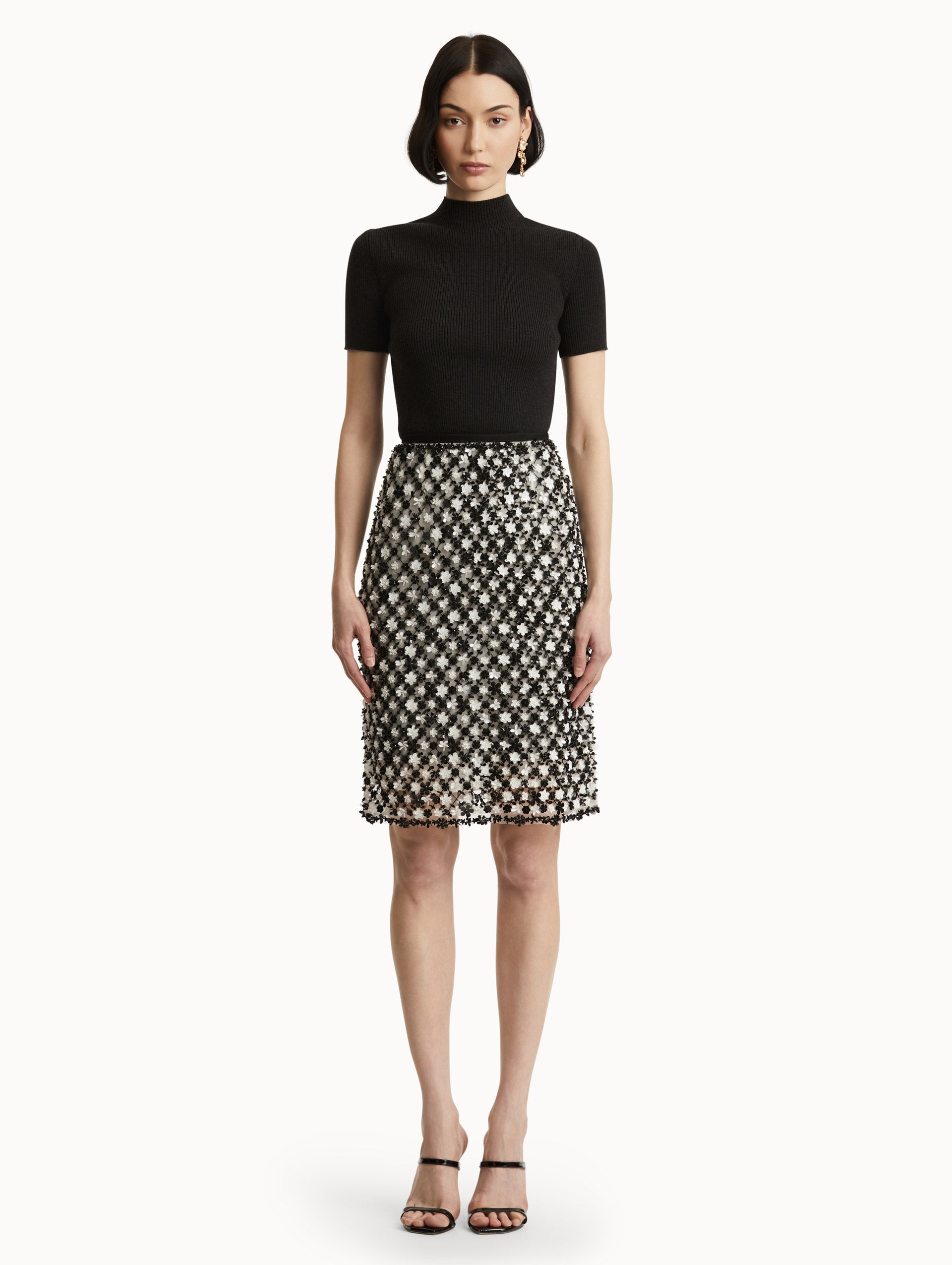 Full body front view of model wearing a high waisted black and ivory floral embroidered pencil skirt that follows a tweed pattern.  