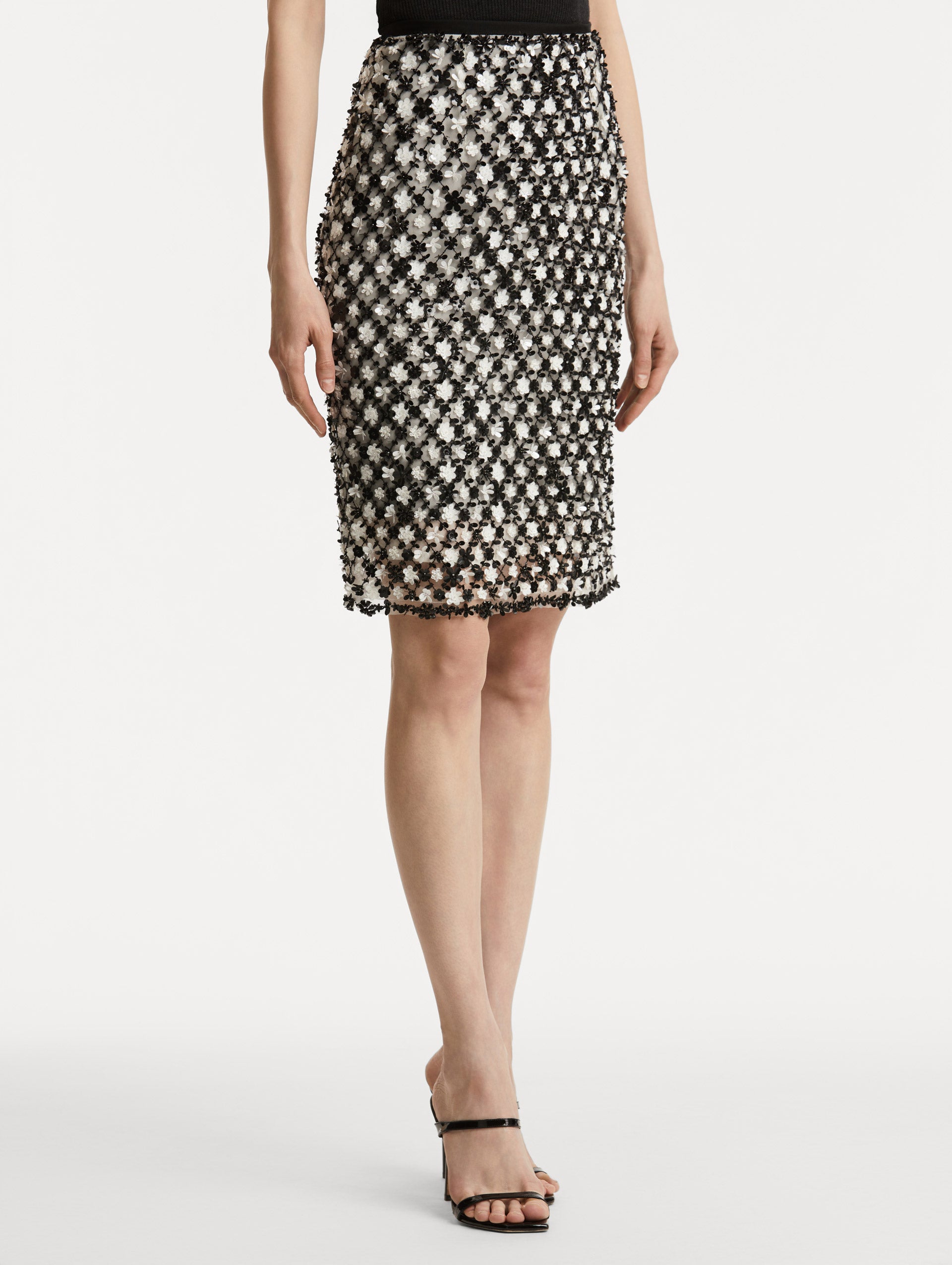 Side view of model wearing a high waisted black and ivory floral embroidered pencil skirt that follows a tweed pattern.  