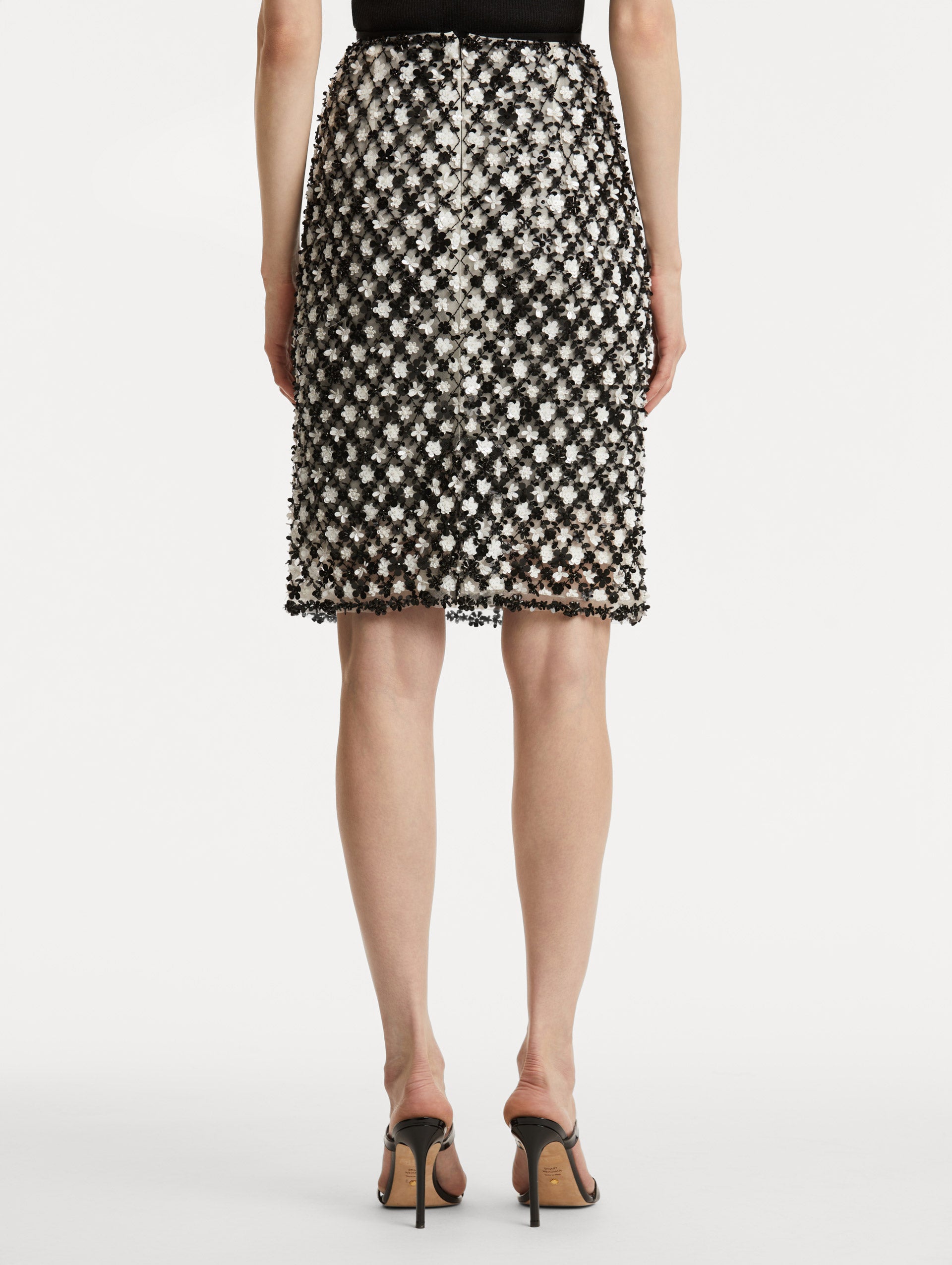 Back view of model wearing a high waisted black and ivory floral embroidered pencil skirt that follows a tweed pattern.  