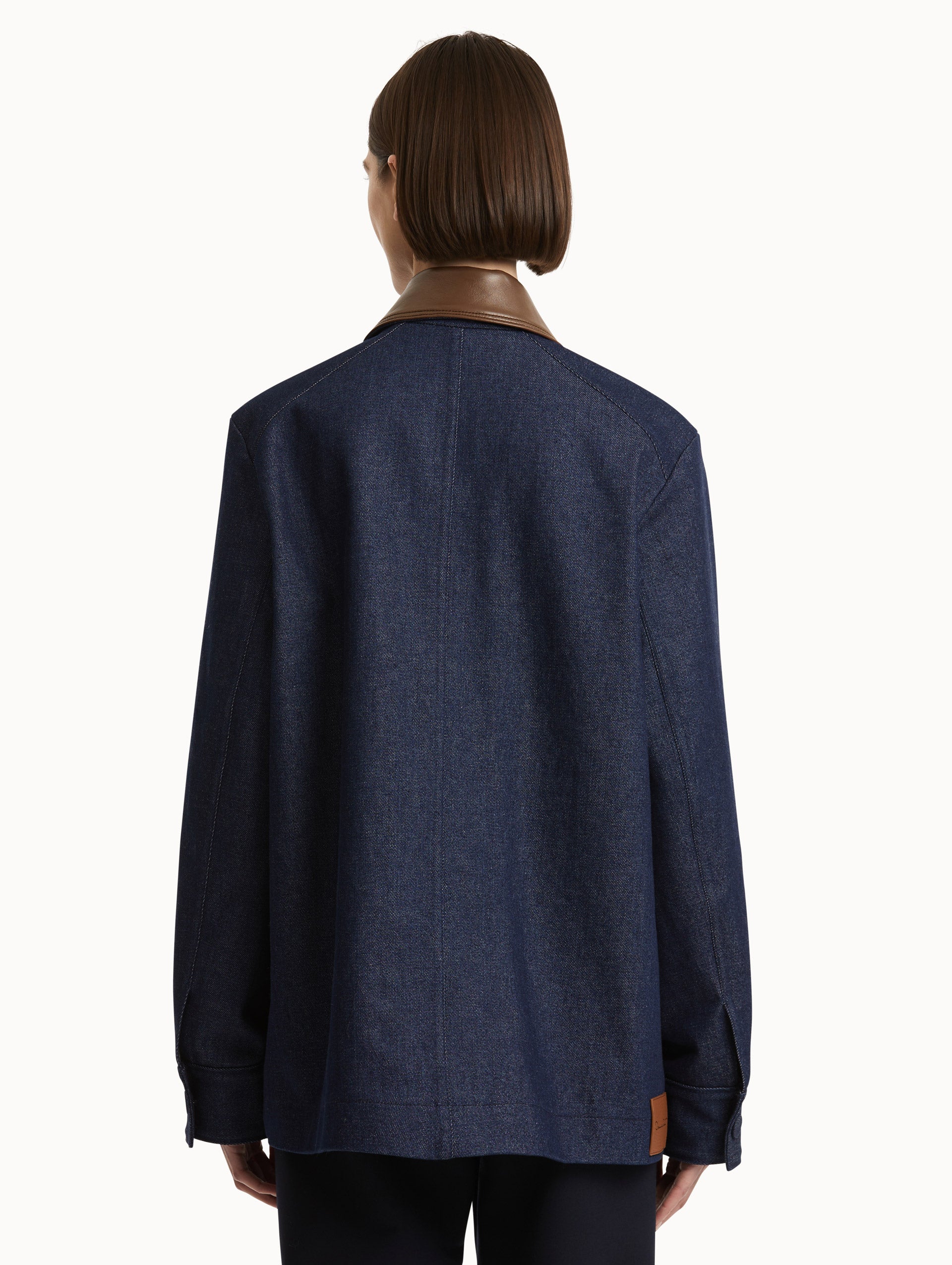 Back view of model wearing dark denim jacket with contrasting brown leather spread collar.