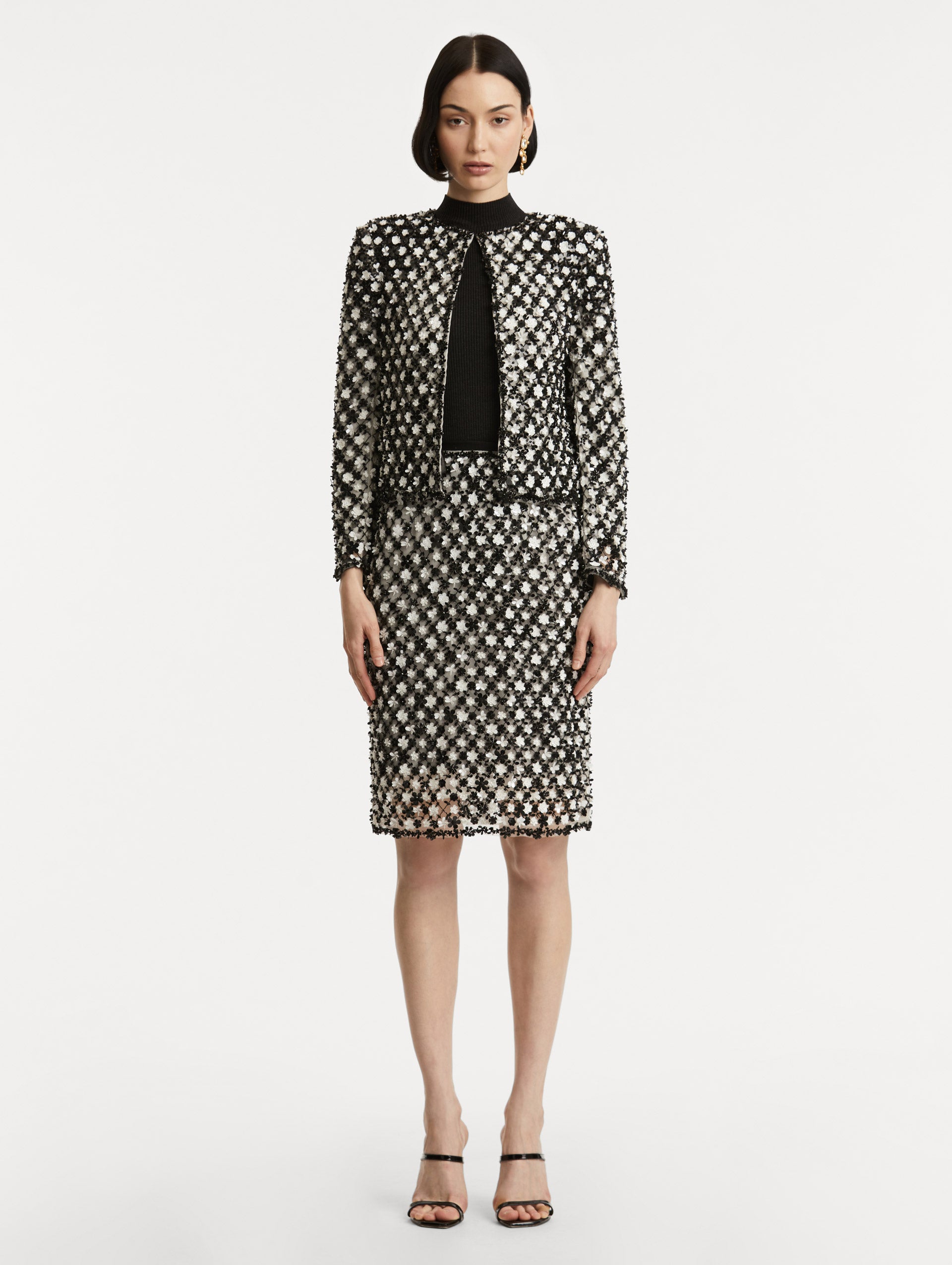 Full body front view of model wearing black and ivory long sleeve jacket with sequin embroidery, where florets create a tweed pattern.