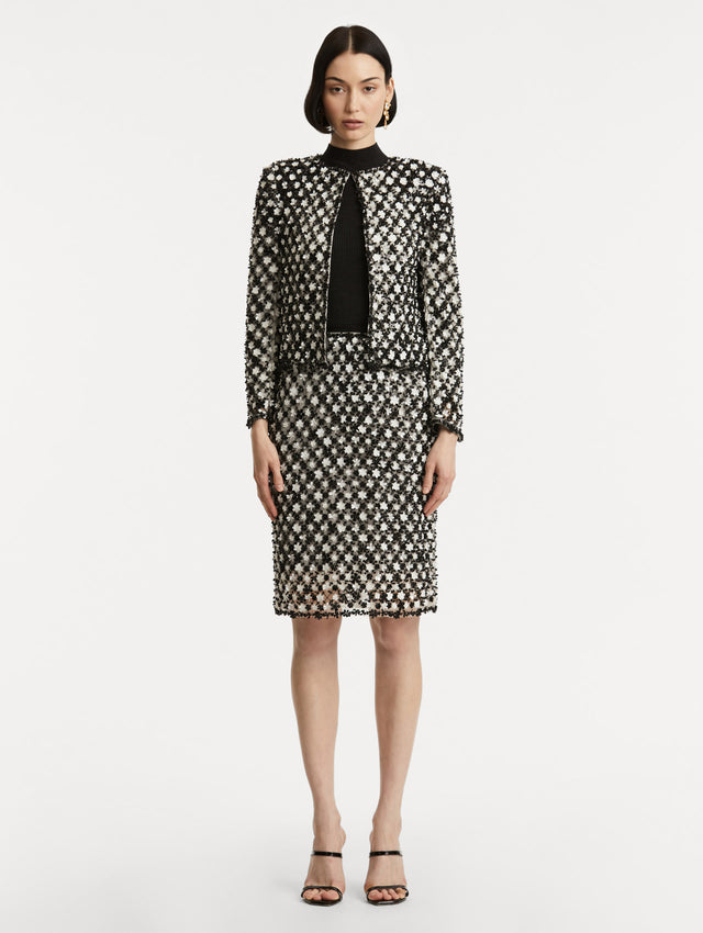 Full body front view of model wearing black and ivory long sleeve jacket with sequin embroidery, where florets create a tweed pattern.