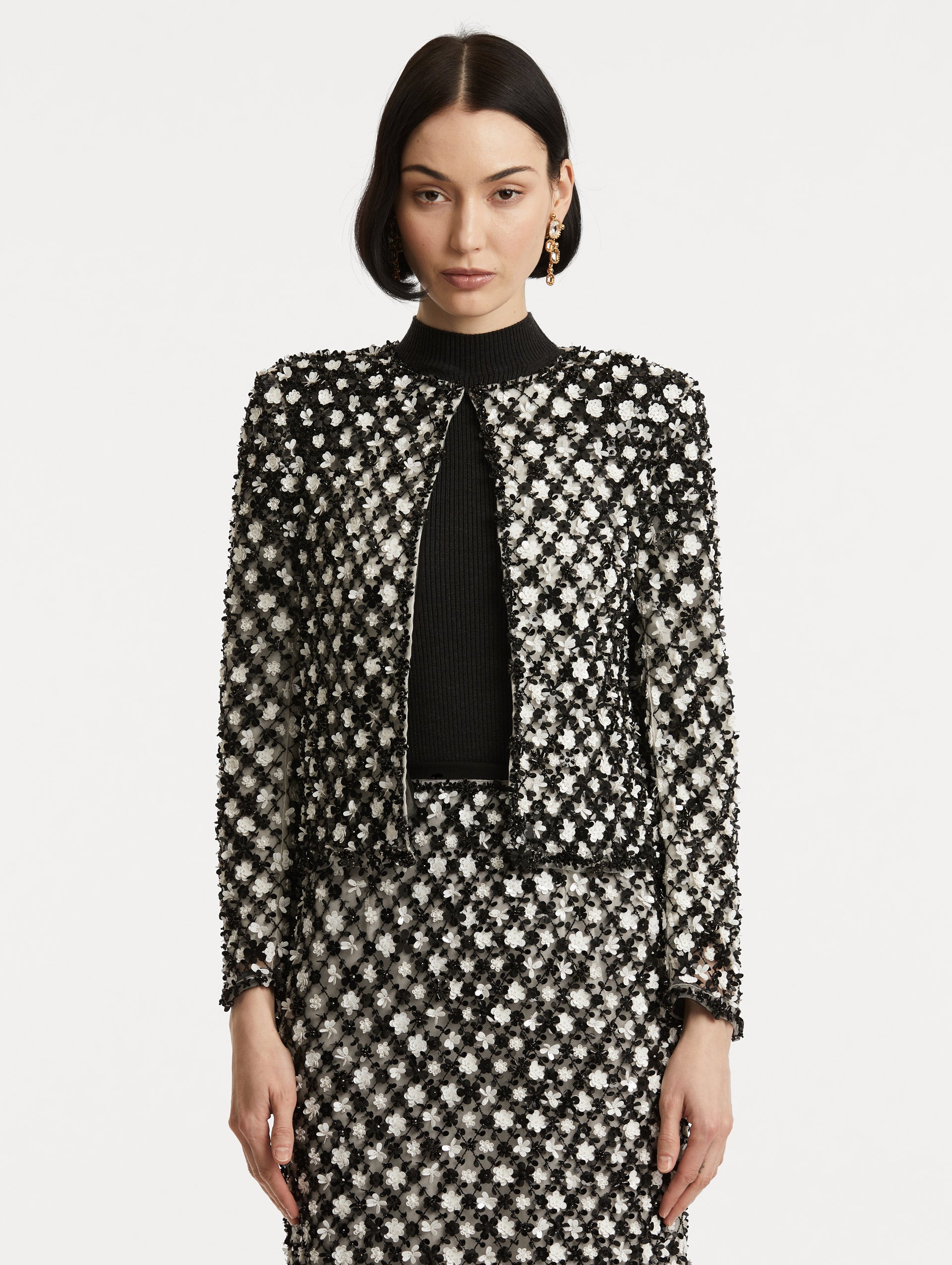 Front view of model wearing black and ivory long sleeve jacket with sequin embroidery, where florets create a tweed pattern.
