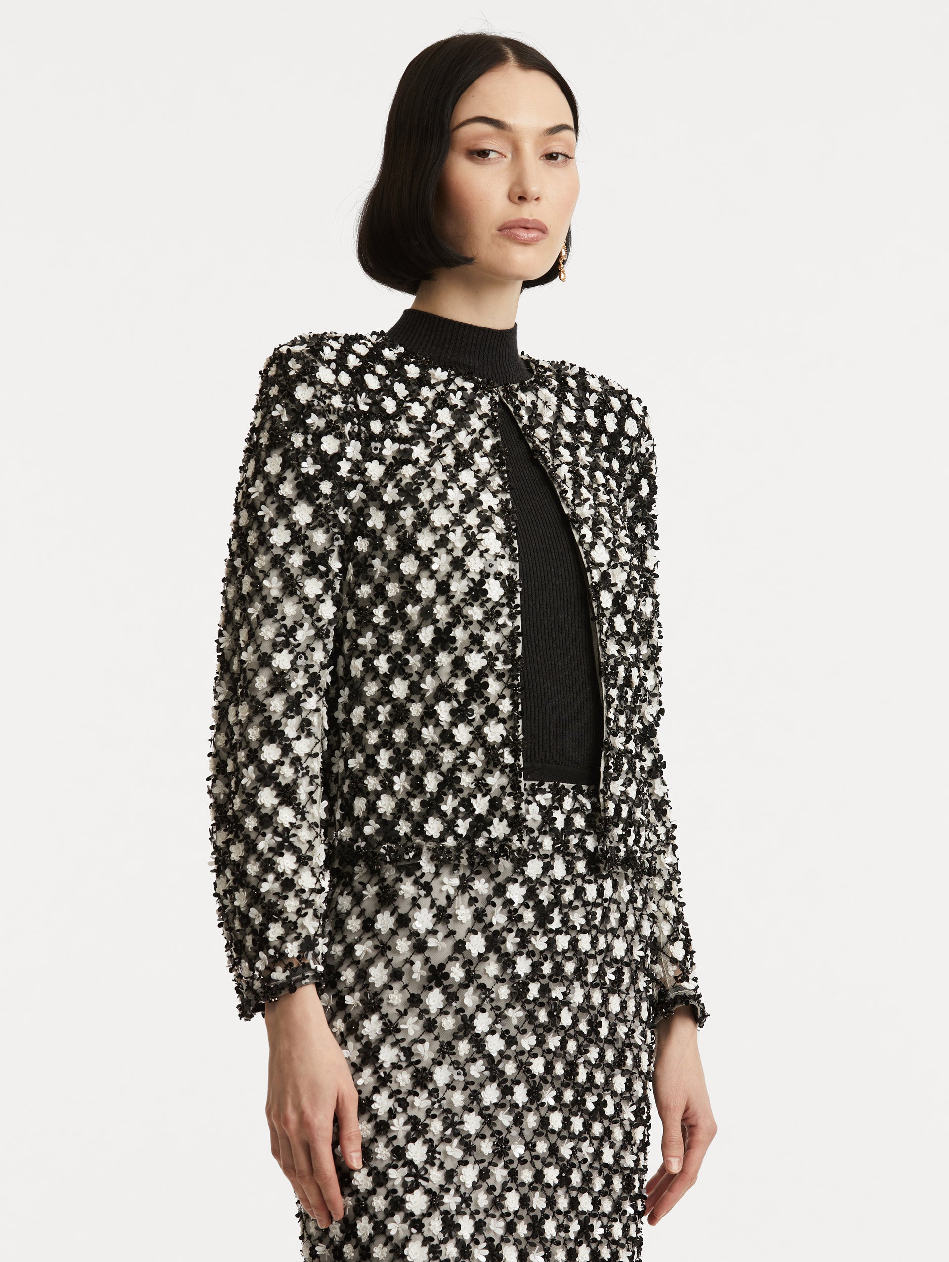 Side view of model wearing black and ivory long sleeve jacket with sequin embroidery, where florets create a tweed pattern.