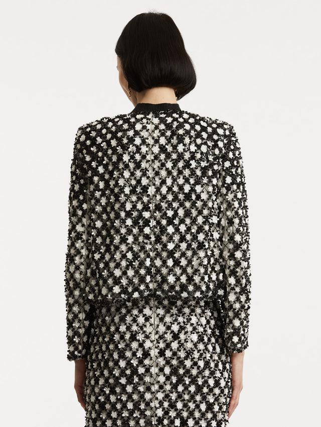 Back view of model wearing black and ivory long sleeve jacket with sequin embroidery, where florets create a tweed pattern.