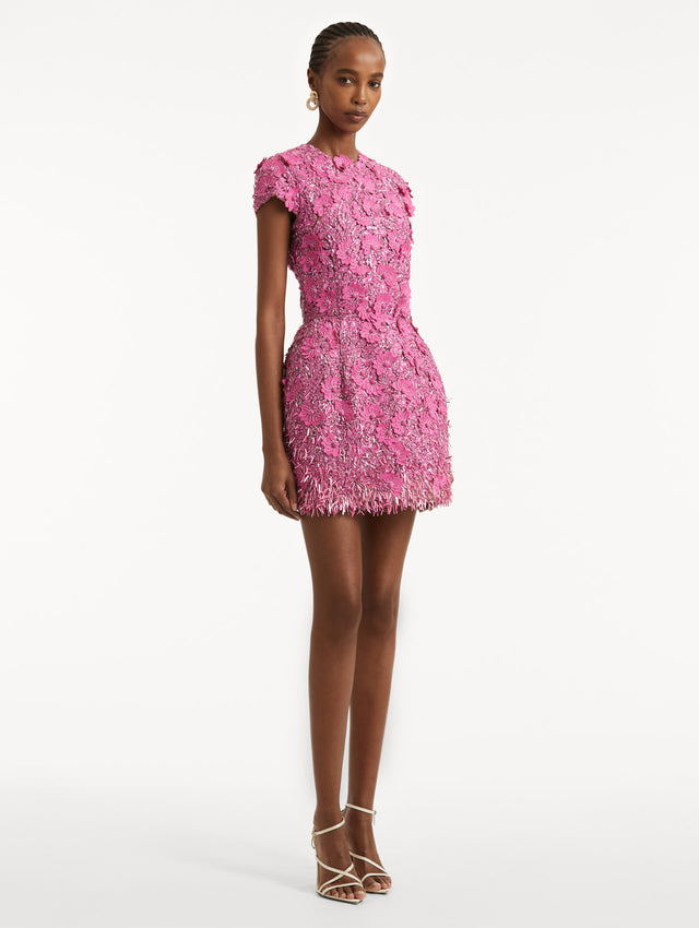 Full body side view of model wearing a pink cocktail mini with floral sequin embroidery and jewel neckline. With short sleeves and a cupcake silhouette.