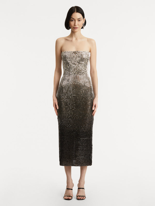 Full body front view of model wearing a strapless dress with a gradient of silver ombré embroidery, the sequins transition from silver to deep black
