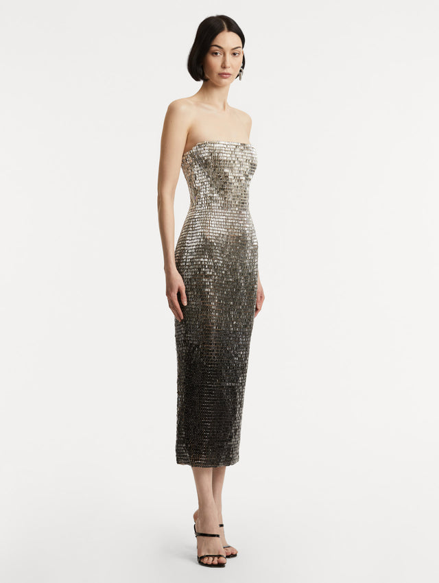 Full body side view of model wearing a strapless dress with a gradient of silver ombré embroidery, the sequins transition from silver to deep black