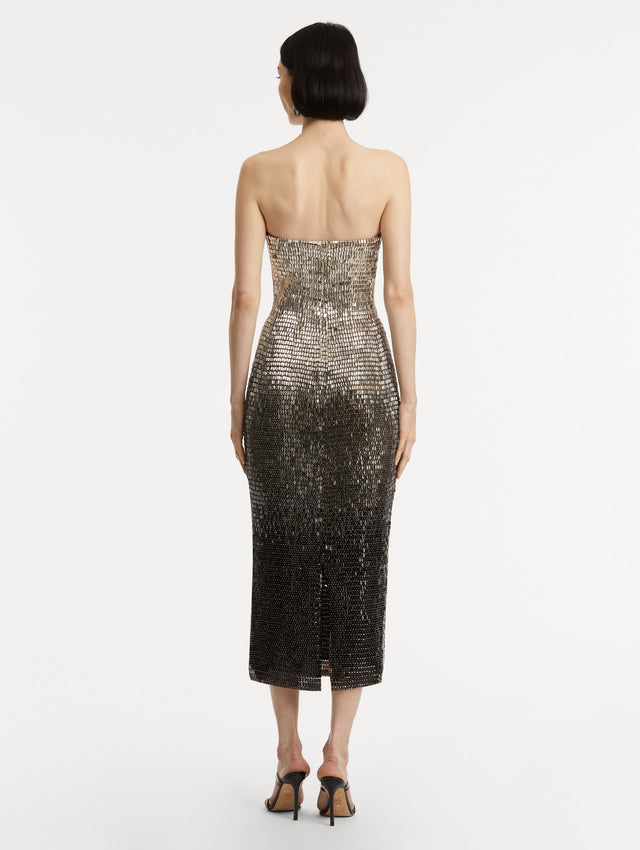 Full body back view of model wearing a strapless dress with a gradient of silver ombré embroidery, the sequins transition from silver to deep black.