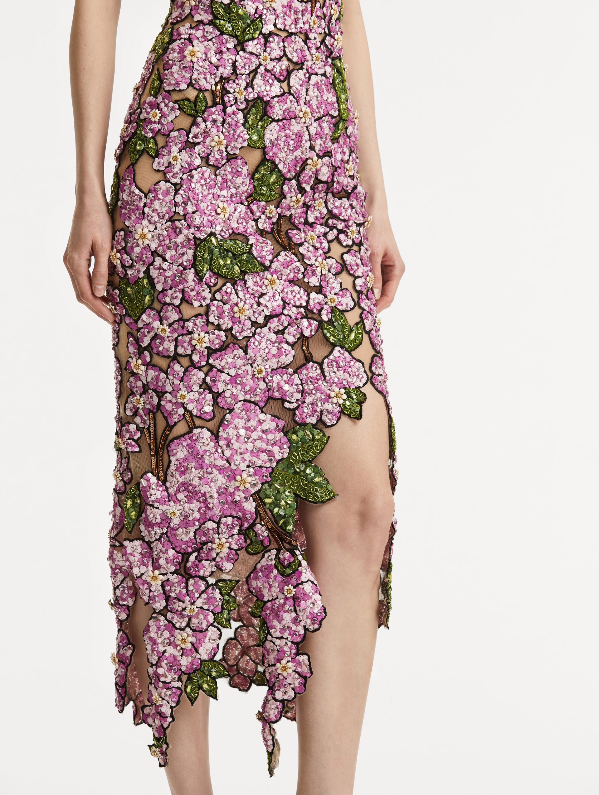 Zoomed in image of the asymmetrical skirt hem with embroidered pink flowers and green leaves on a sheer tulle base. 