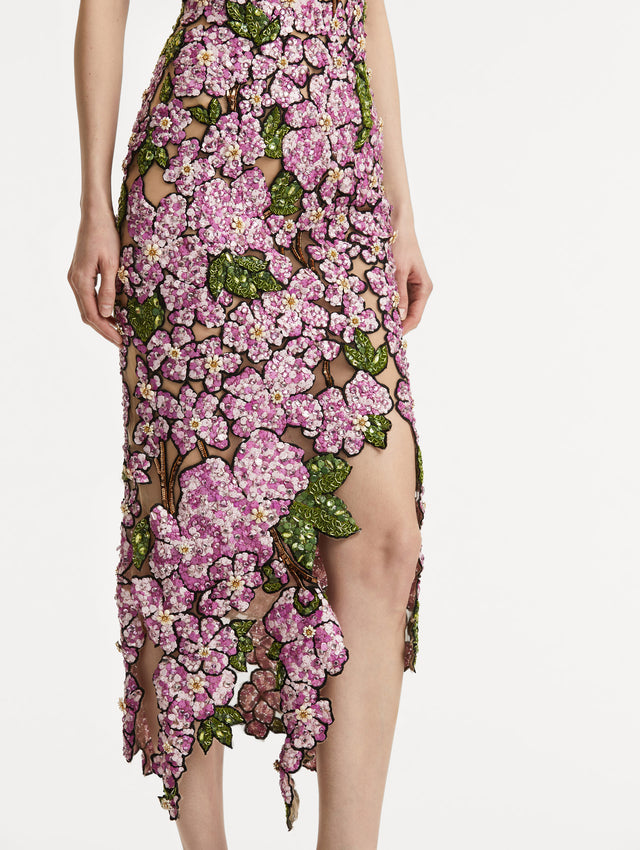 Zoomed in image of the asymmetrical skirt hem with embroidered pink flowers and green leaves on a sheer tulle base. 