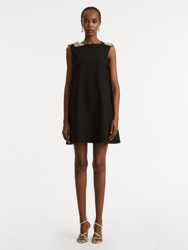 Full body front view of model wearing a black wool minidress in a shift silhouette that features silver sequin fern embroidery on the shoulders. 