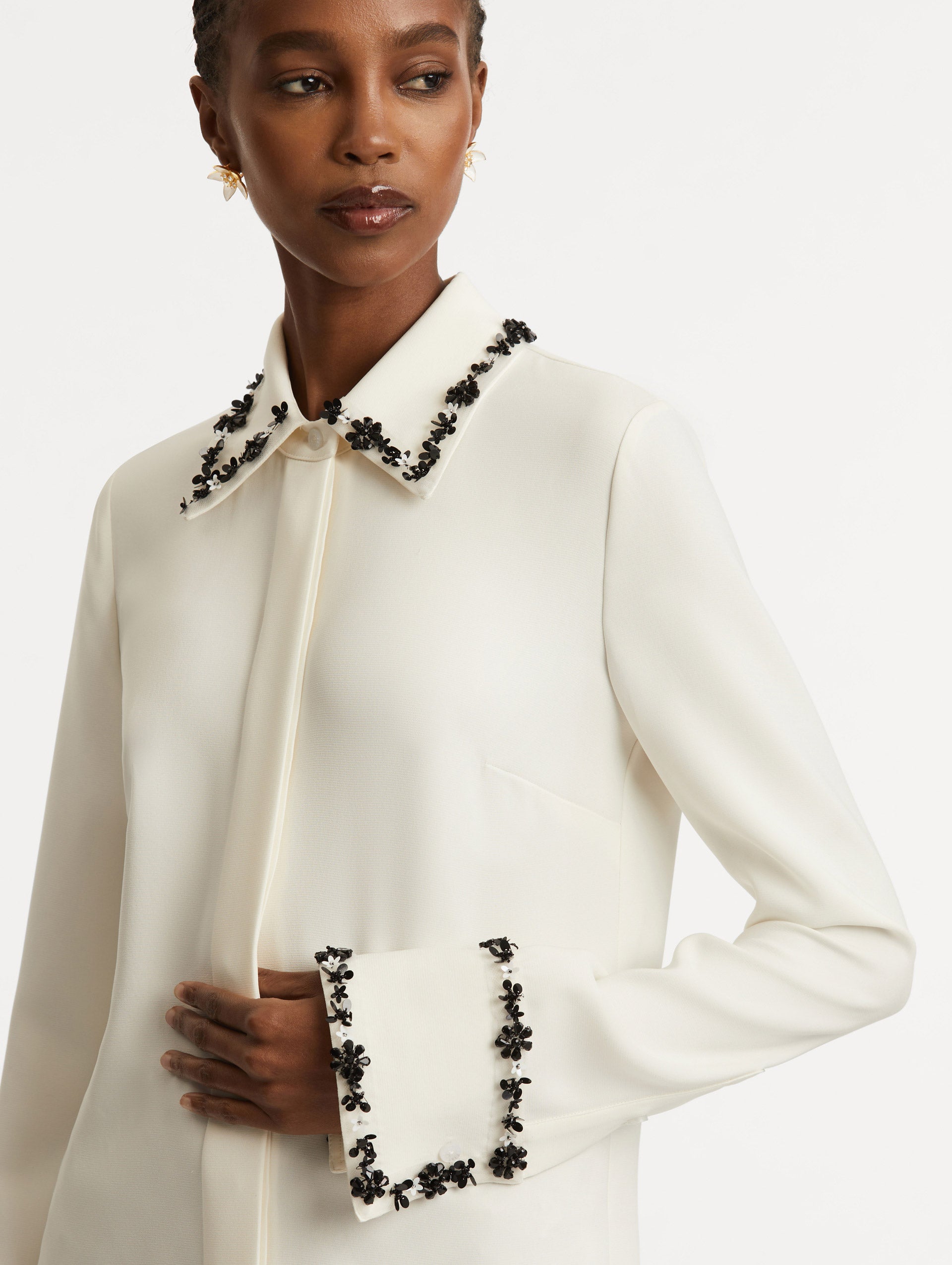 Zoomed in image of black sequin flower embroidery that traces the trim with a spread collar on an ivory blouse.