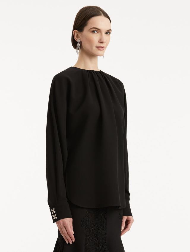 Side view of model wearing black long sleeve top with crystal floral cuff appliques. 