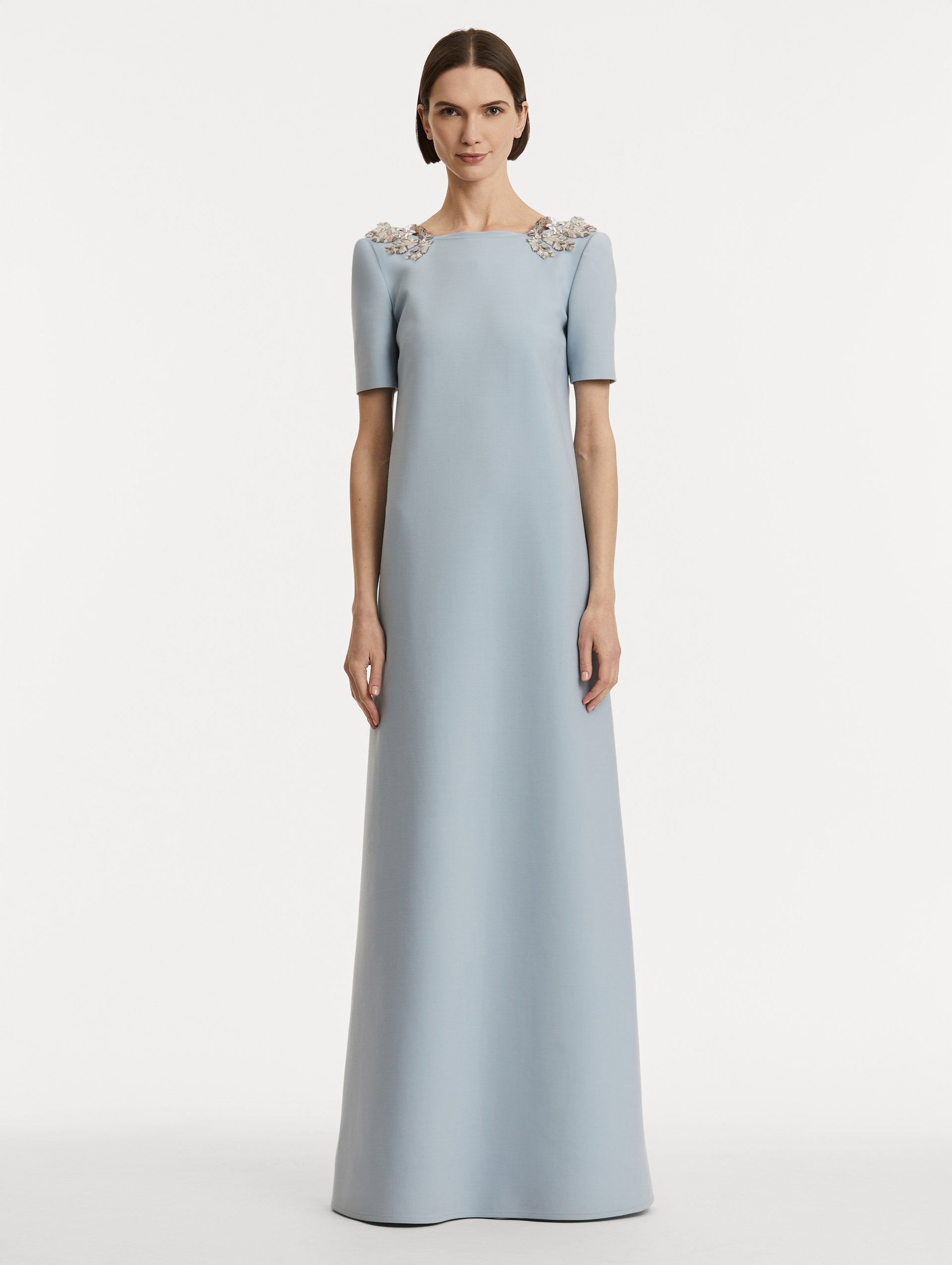 Full body front view of model wearing light blue wool caftan features short sleeves with silver fern embroidery sequins on the shoulders. 