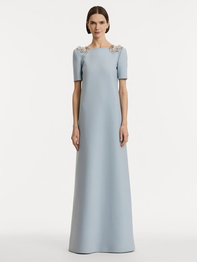 Full body front view of model wearing light blue wool caftan features short sleeves with silver fern embroidery sequins on the shoulders. 