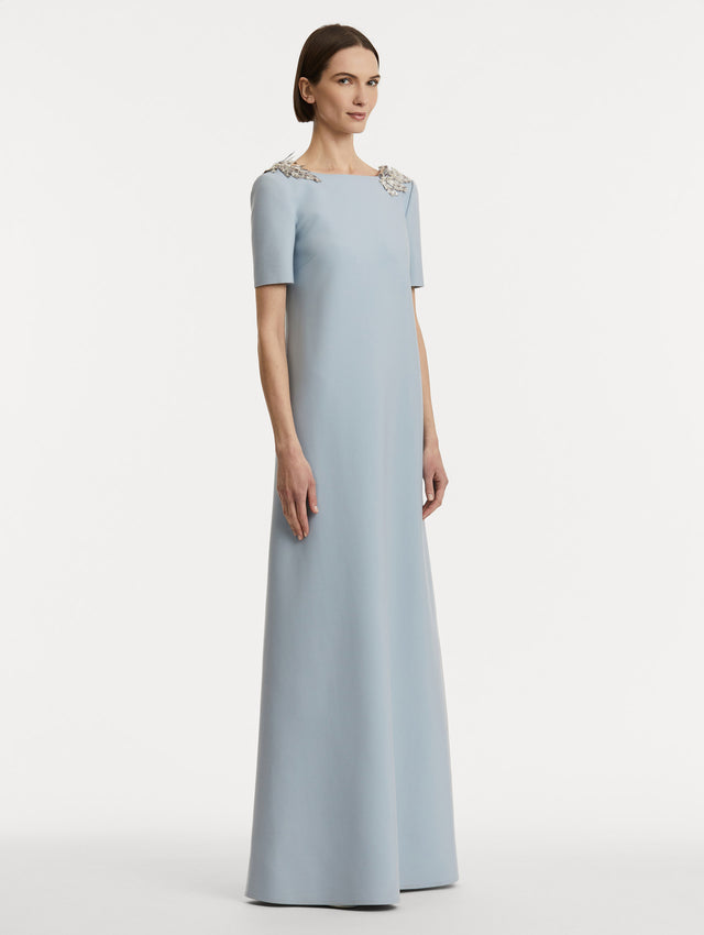 Full body Side view of model wearing light blue wool caftan features short sleeves with silver fern embroidery sequins on the shoulders. 