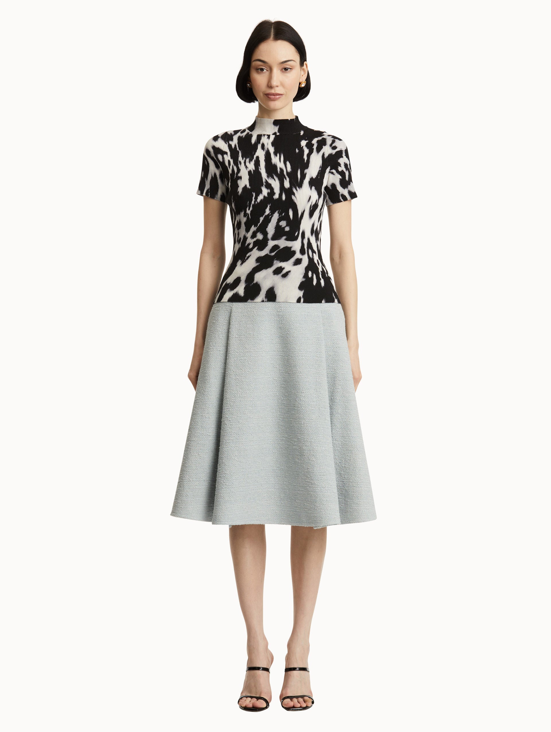 Full body front view of model wearing short sleeve ribbed knit pullover with a mock neckline and cow print in ecru and black. 