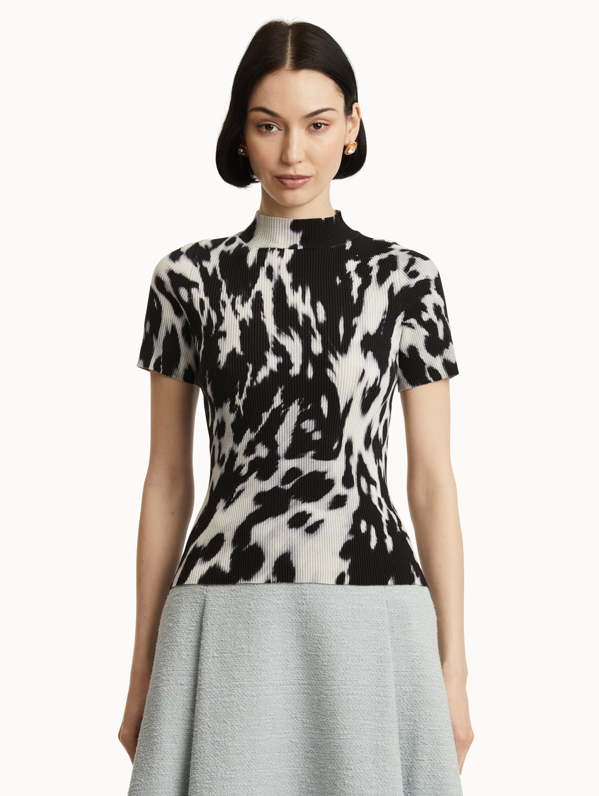 Front view of model wearing short sleeve ribbed knit pullover with a mock neckline and cow print in ecru and black. 