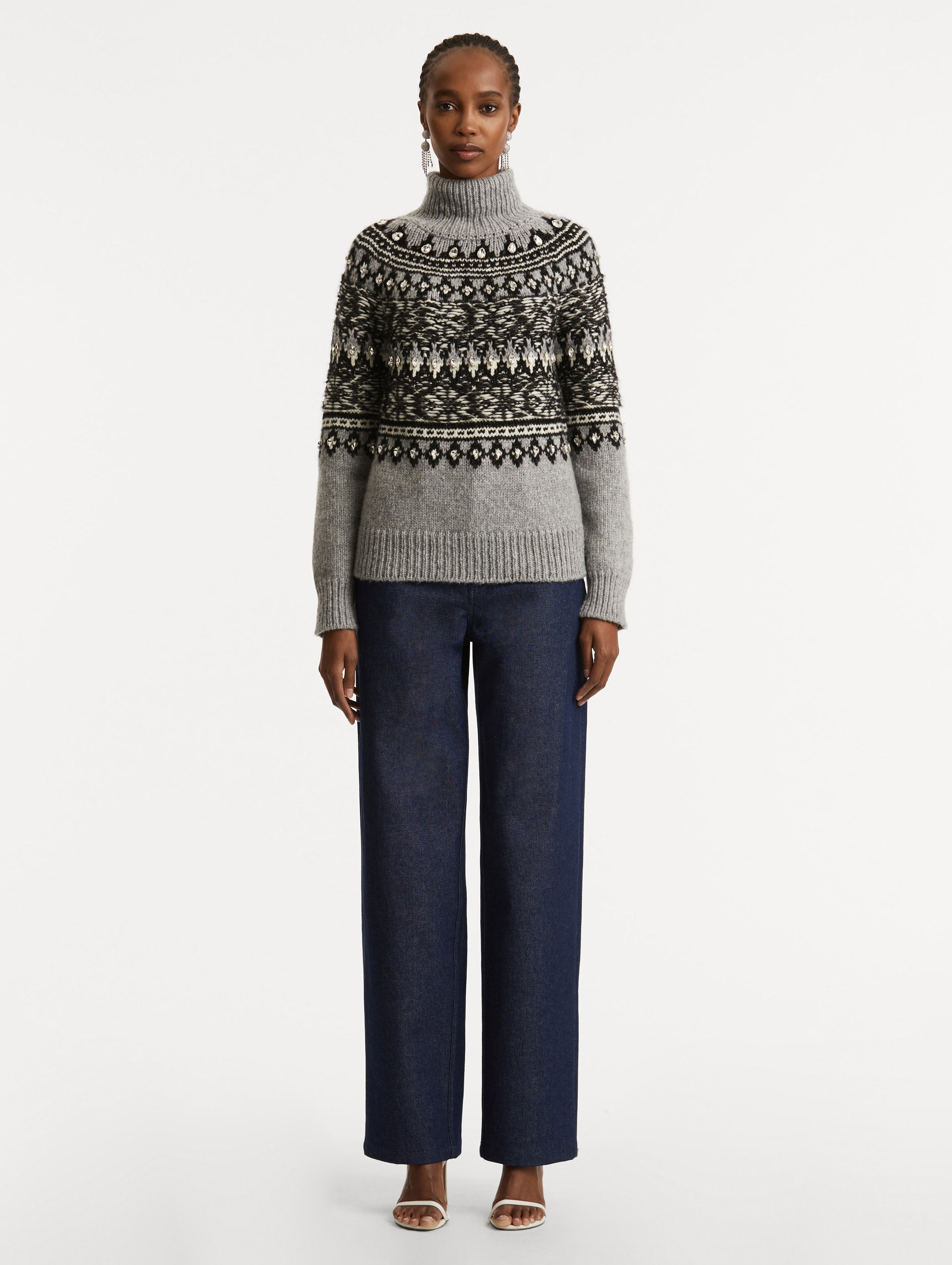 Full body front view of model wearing long sleeve grey turtle neck pullover with crystal embroidery and black patterns. 