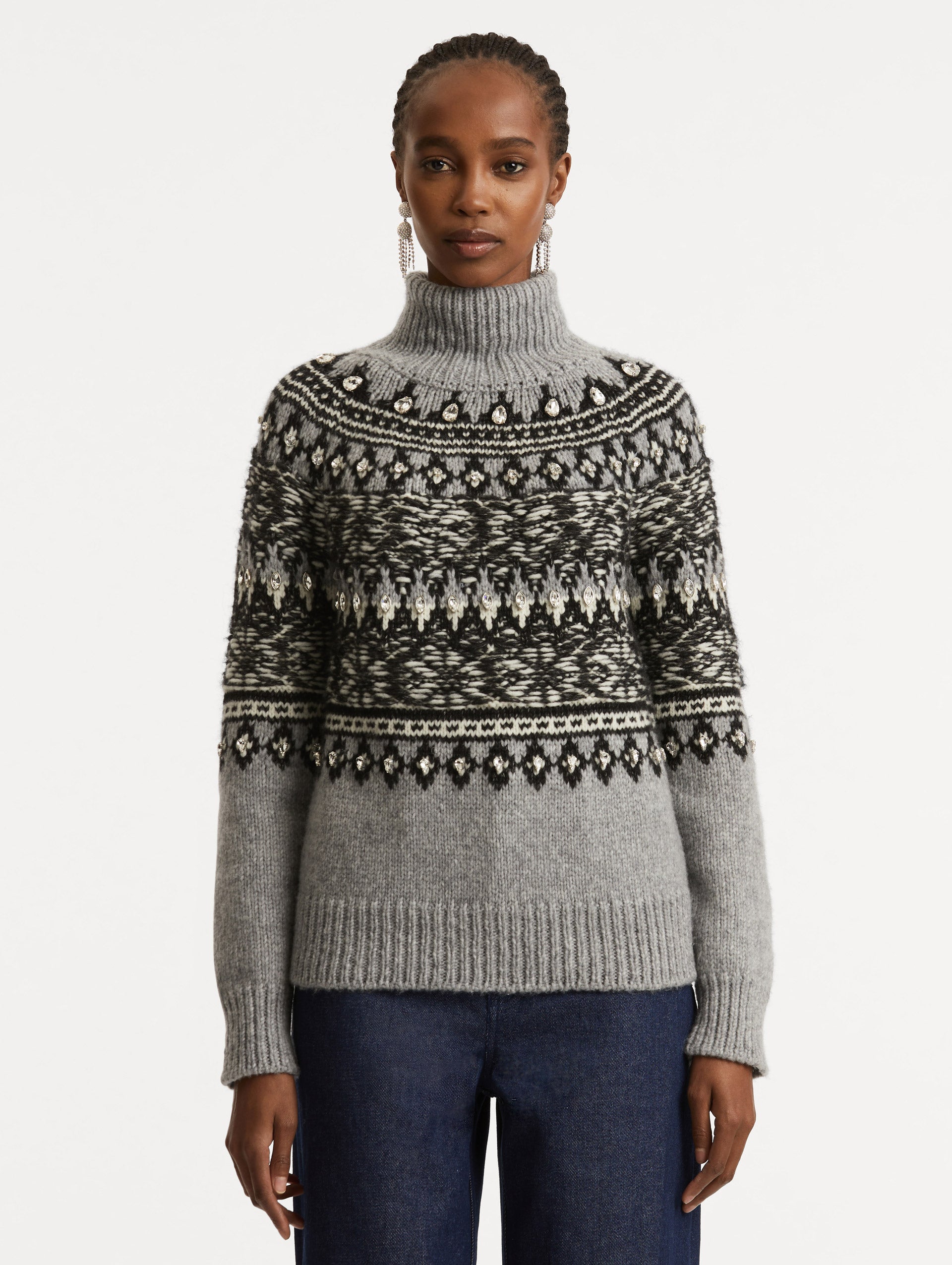 Front view of model wearing long sleeve grey turtle neck pullover with crystal embroidery and black patterns. 