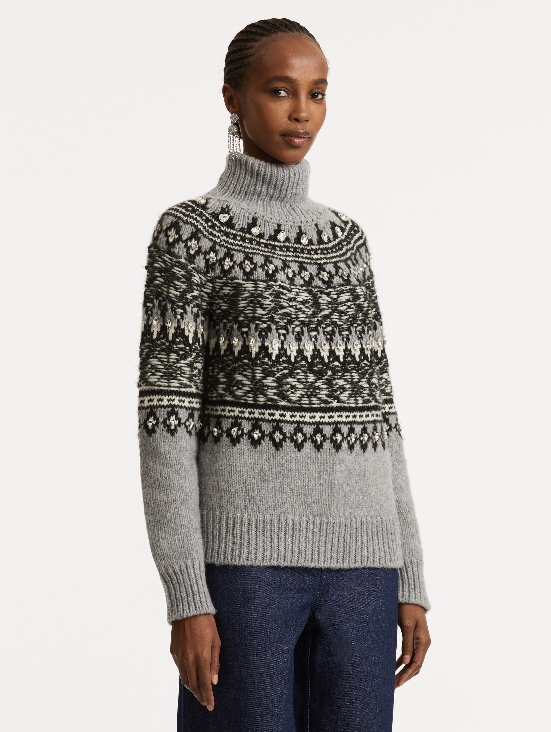 Side view of model wearing long sleeve grey turtle neck pullover with crystal embroidery and black patterns. 