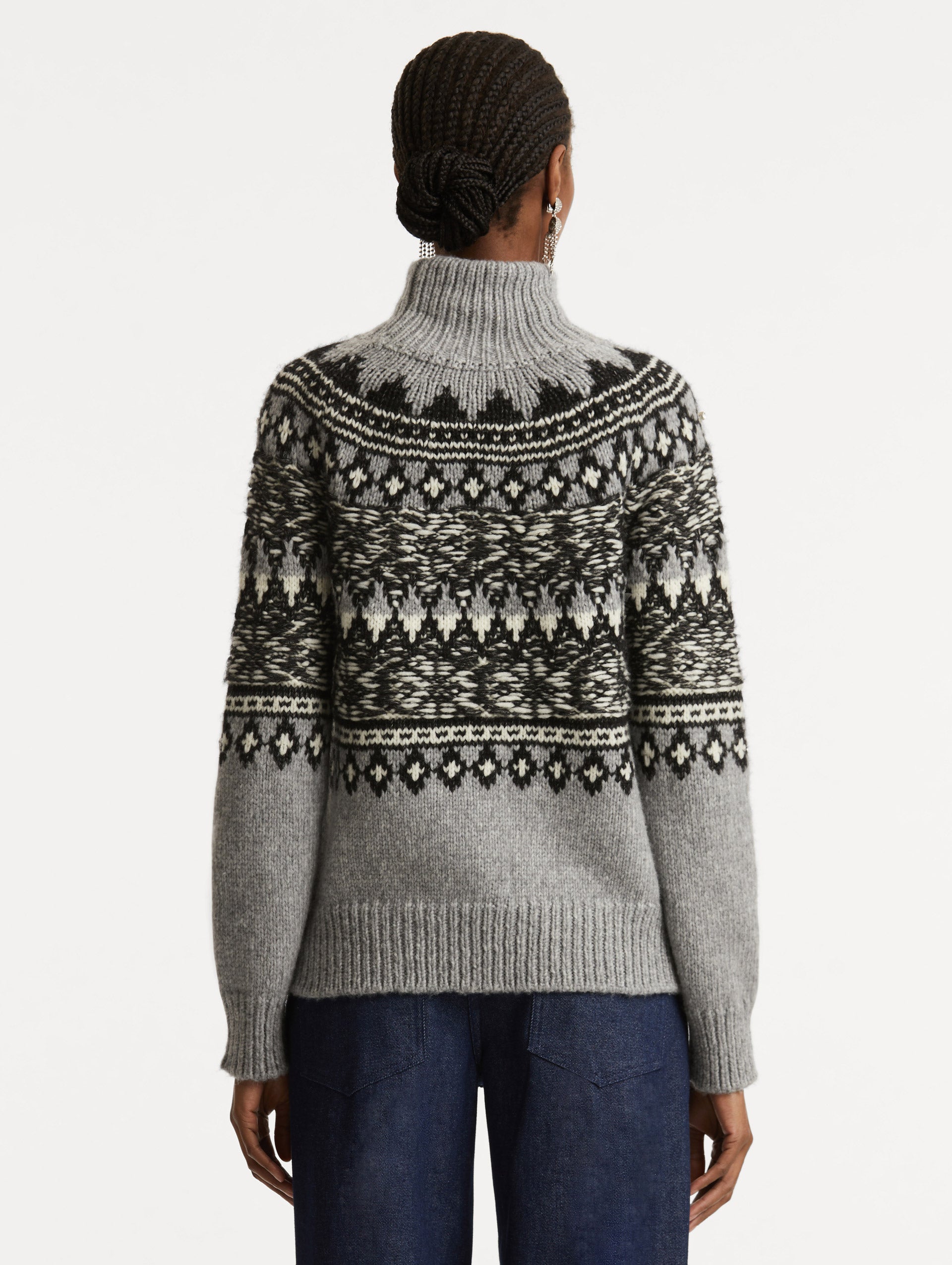 Full body back view of model wearing long sleeve grey turtle neck pullover with crystal embroidery and black patterns. 
