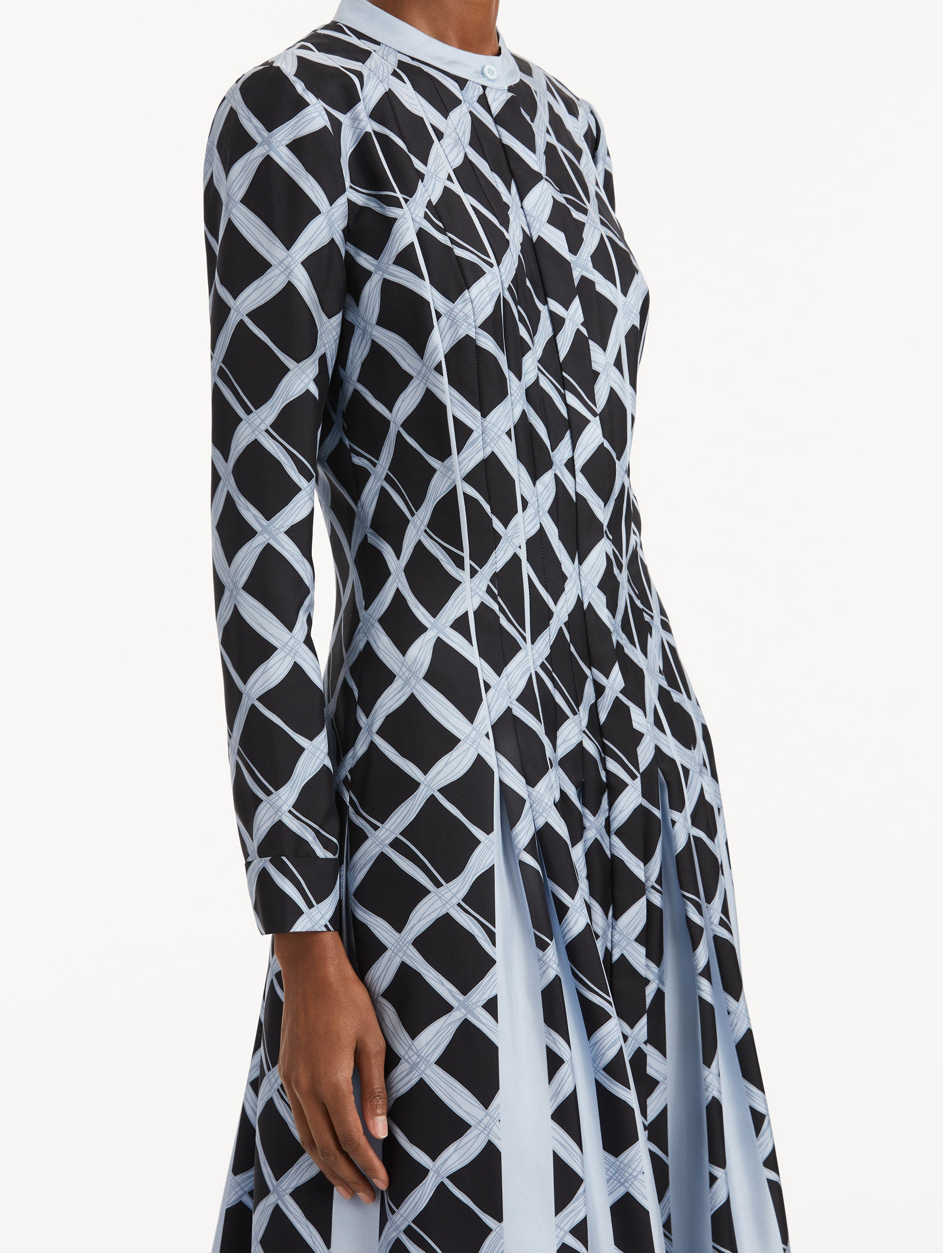 Zoomed in image of long sleeve blue silk dress featuring a grid pattern, pleated bodice while the skirt falls to contrasting insets. 