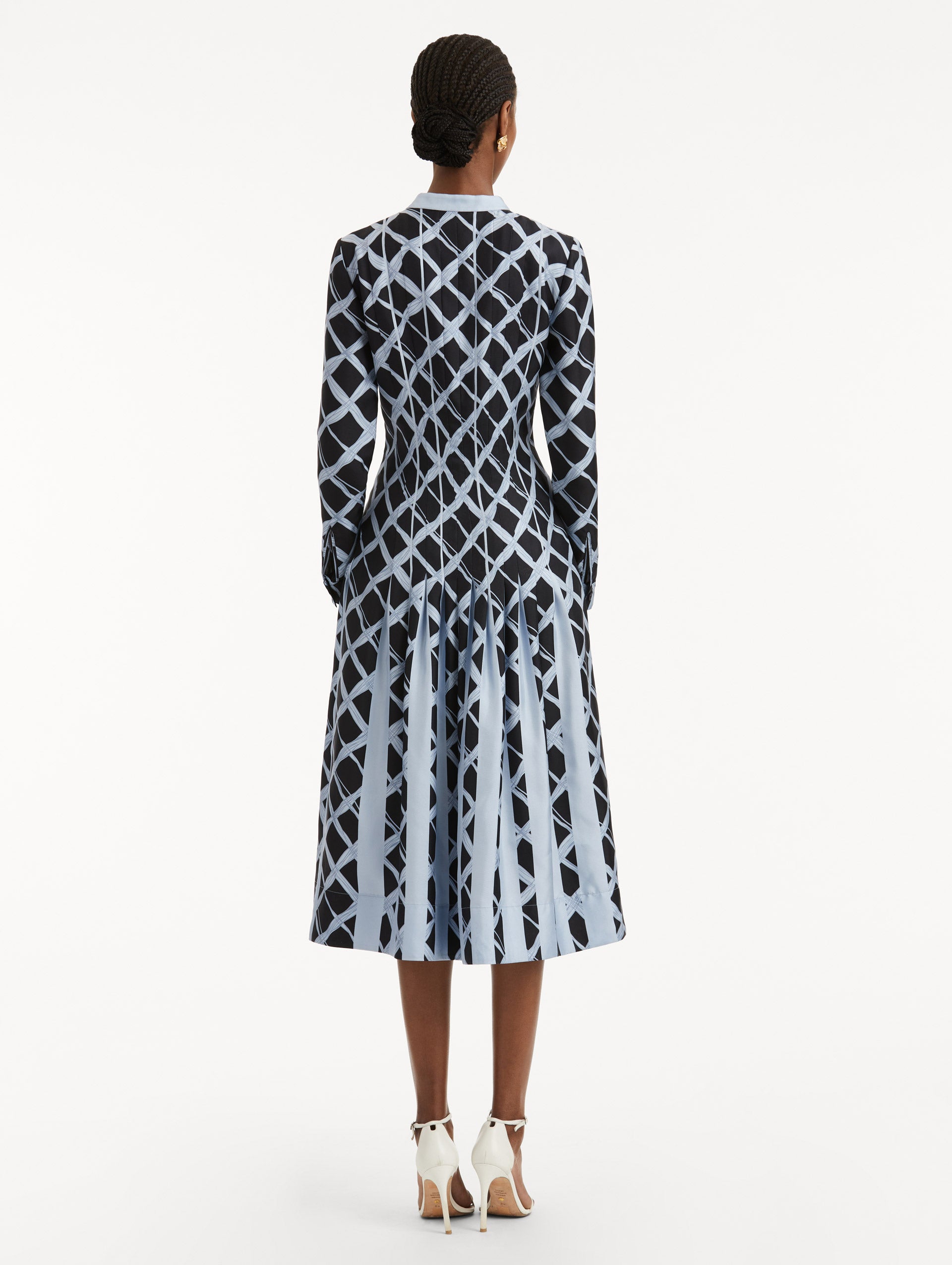 Full body back view of model wearing long sleeve blue silk dress featuring a grid pattern, pleated bodice while the skirt falls to contrasting insets. 