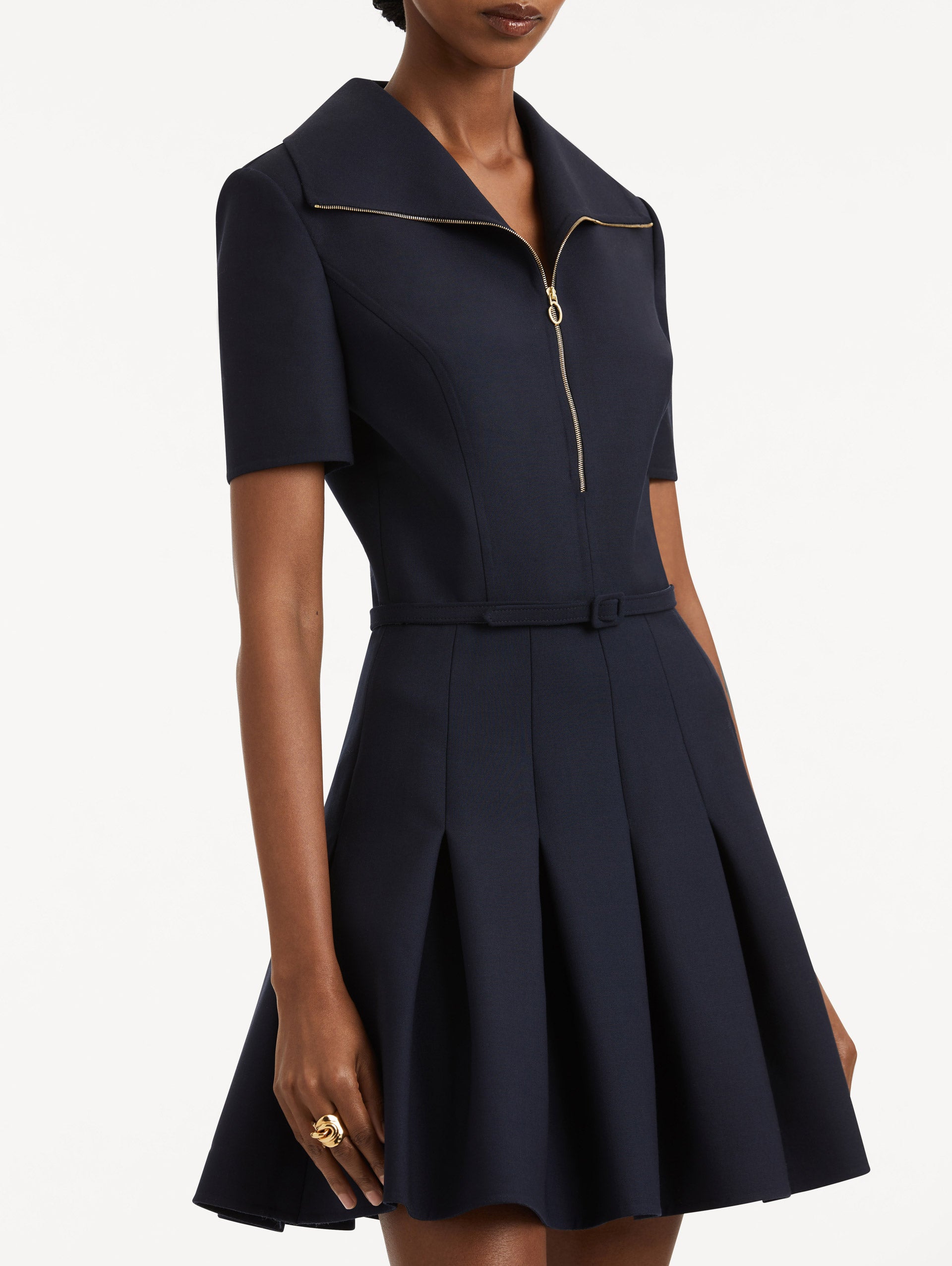 Zoomed in image of navy short sleeve mini dress with gold zipper spread collar, matching self-belt, and pleated skirt. 