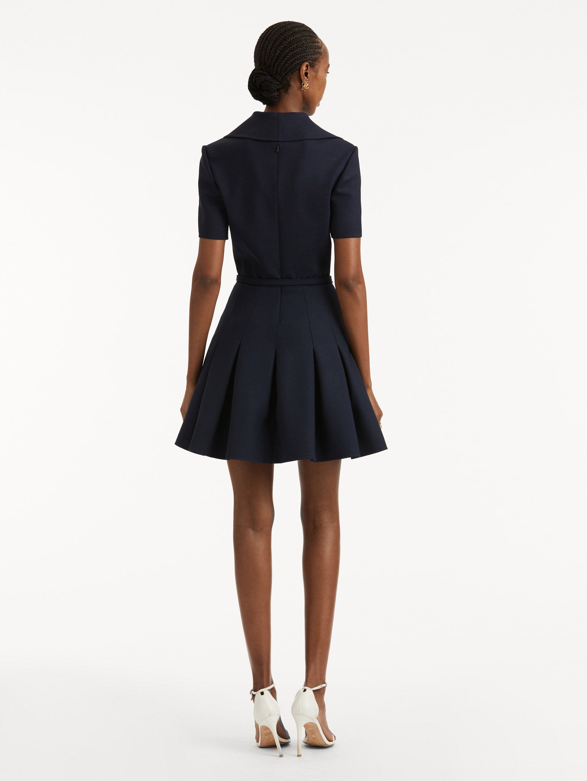 Full body back view of model wearing navy short sleeve mini dress with spread collar, matching self-belt and pleated skirt. 
