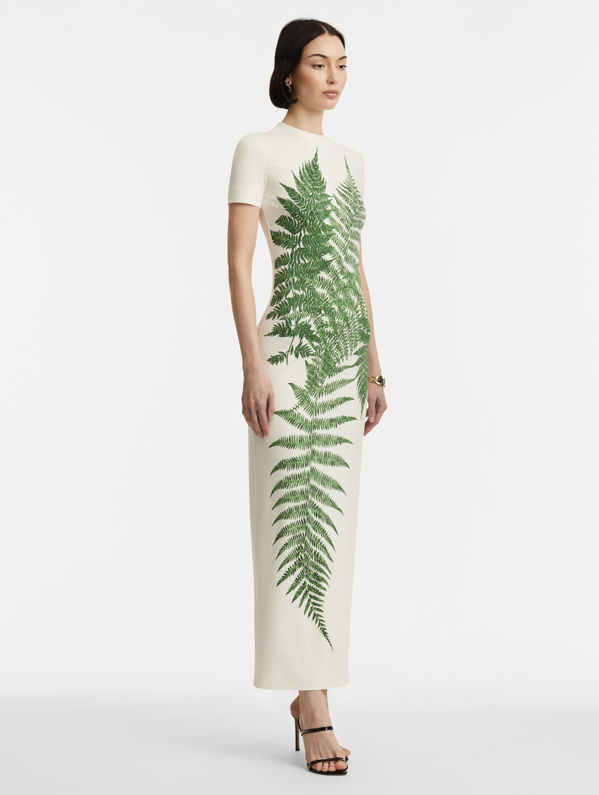 Full body side view of model wearing a short-sleeve jersey dress with a ivory base and green ferns concentrated at the center. 