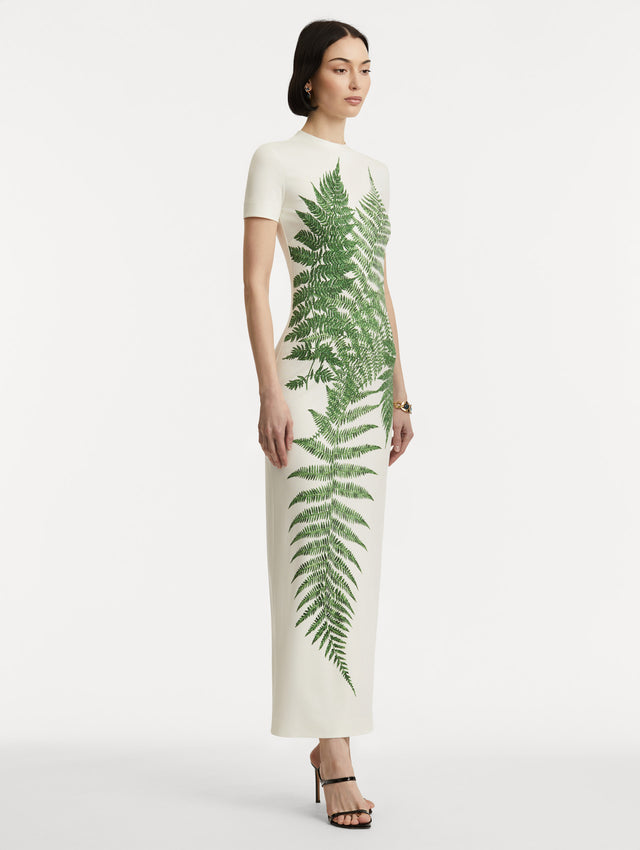 Full body side view of model wearing a short-sleeve jersey dress with a ivory base and green ferns concentrated at the center. 