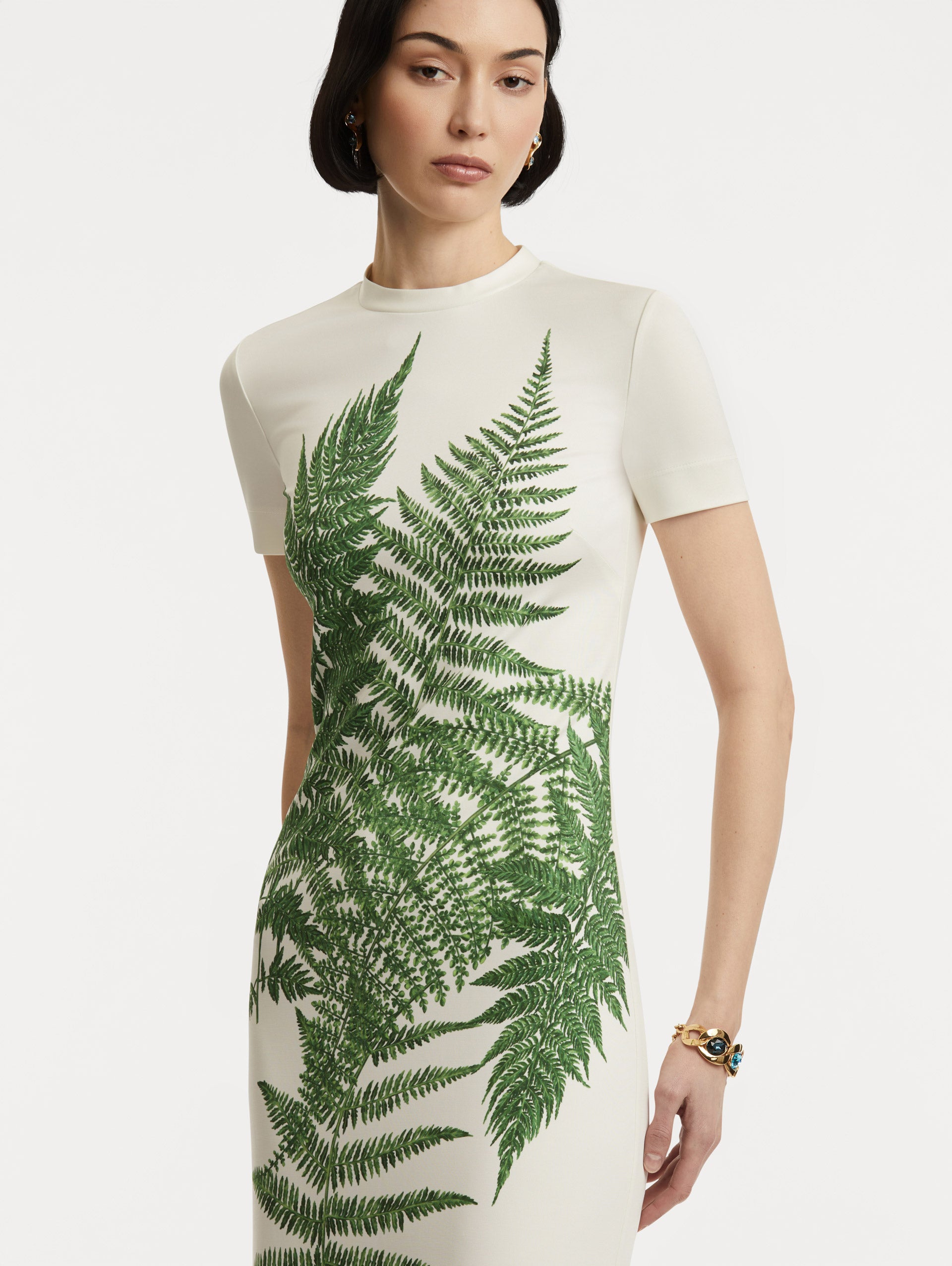 Zoomed in image of model wearing a jersey short-sleeve dress with  ferns concentrated at the center with a ivory back round. 