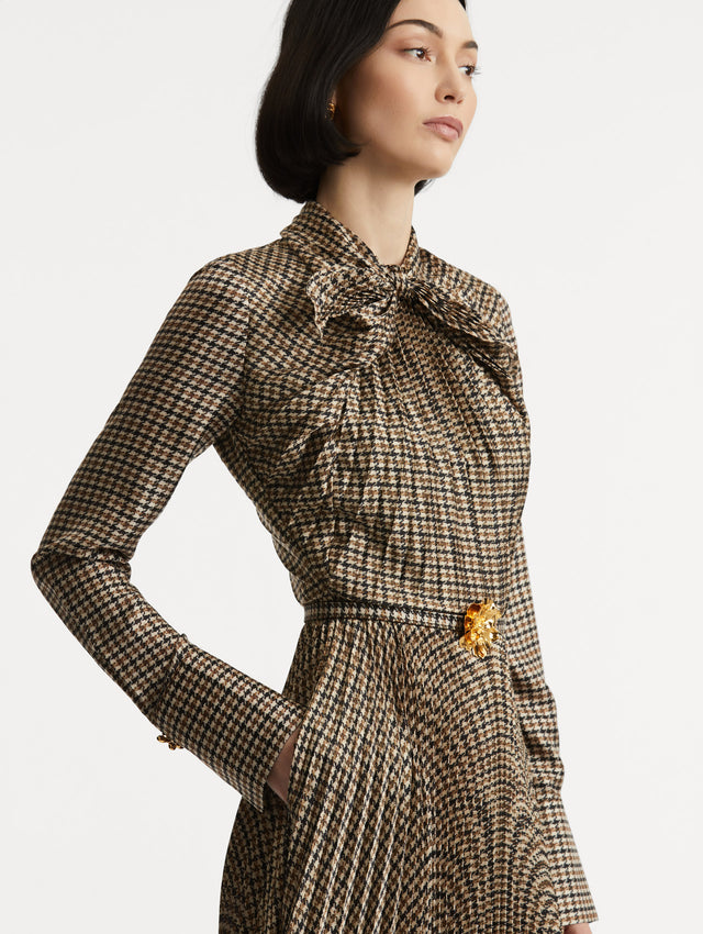 Zoomed in image of multiple brown colored neck tie and dress with side pockets and long sleeves. Dress also features pleating and a matching self-belt with a gold peony at the center. 
