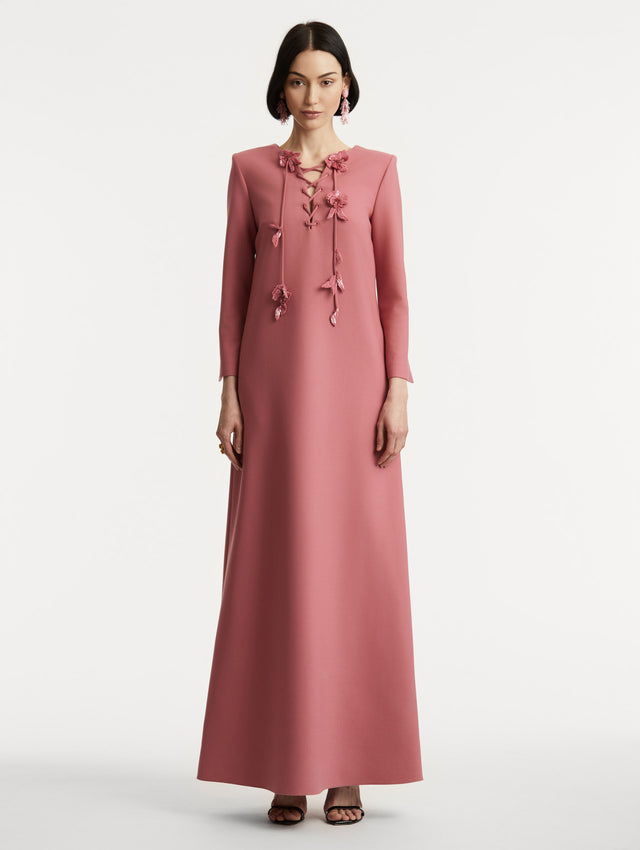 Full body front view of model wearing long sleeve pink caftan with lace up floral detail at the neckline. 