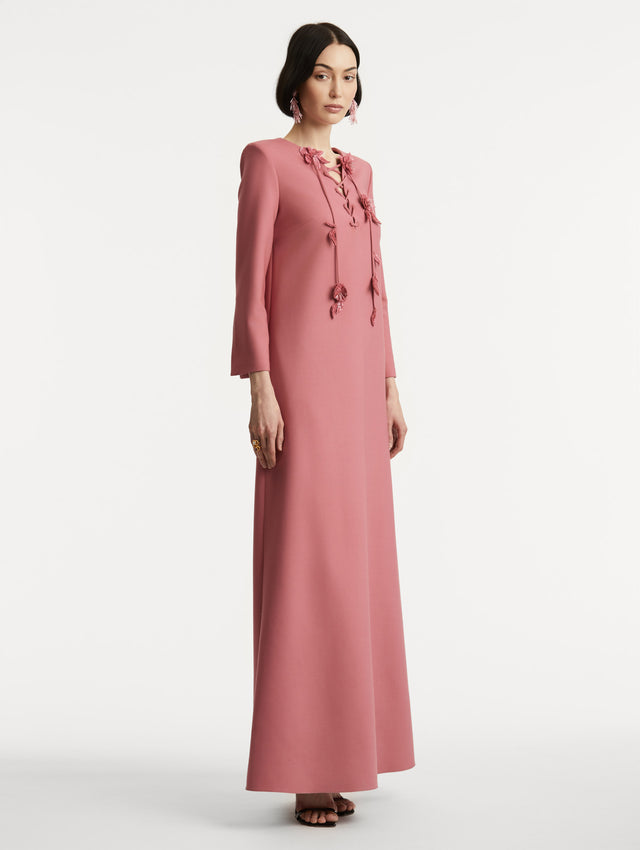 Full body side view of model wearing long sleeve pink caftan with lace up floral detail at the neckline. 
