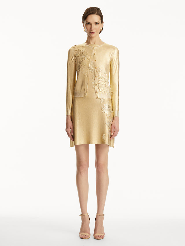 The model is wearing a Metallic gold cardigan with cherry blossom embroidery, over a matching dress. Front view