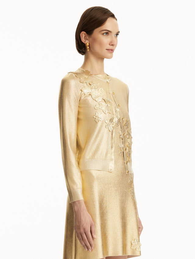 The model is wearing a Metallic gold cardigan with cherry blossom embroidery, over a matching dress. Side view